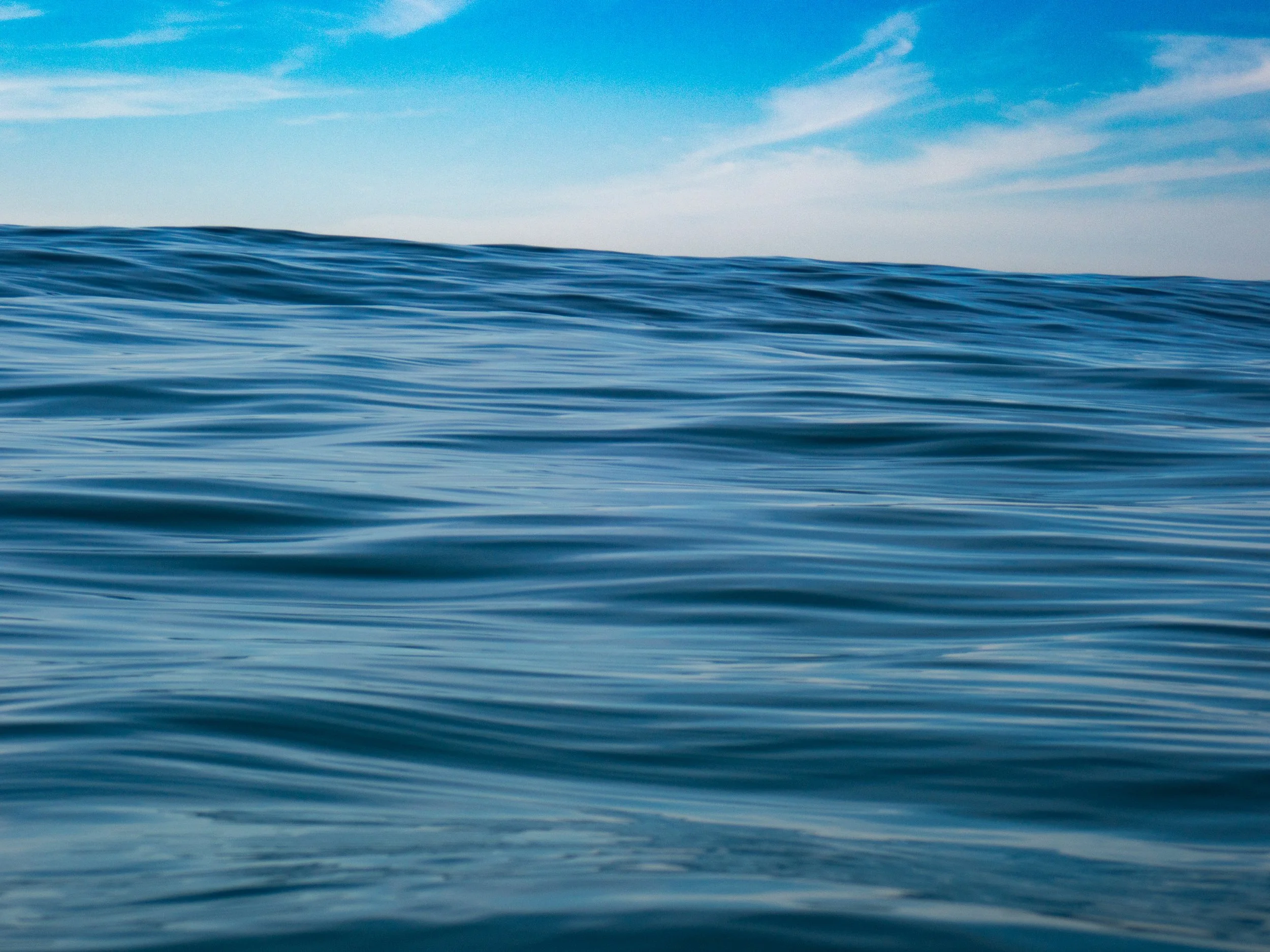 Ocean waves under a blue sky with wispy clouds.