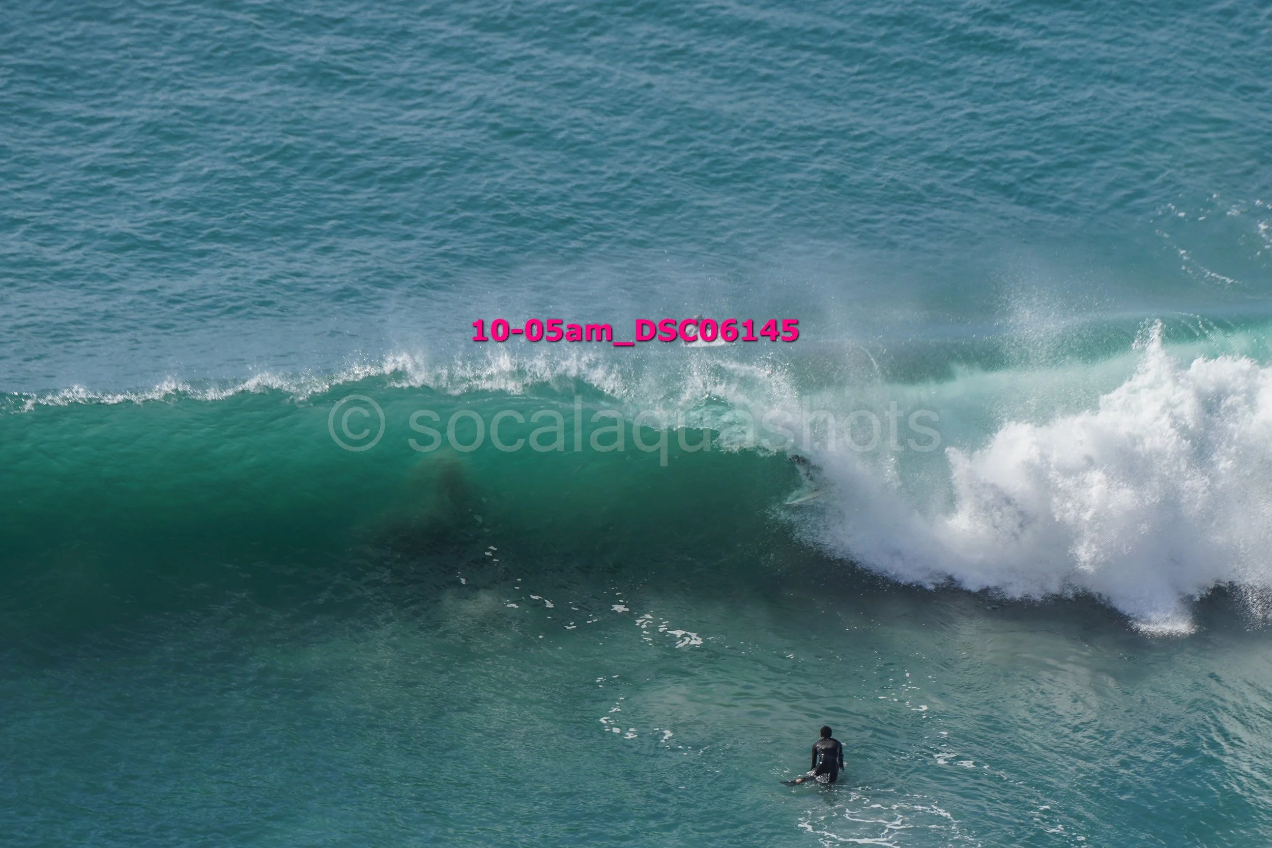 A person surfing on a large ocean wave with blue water in the background.