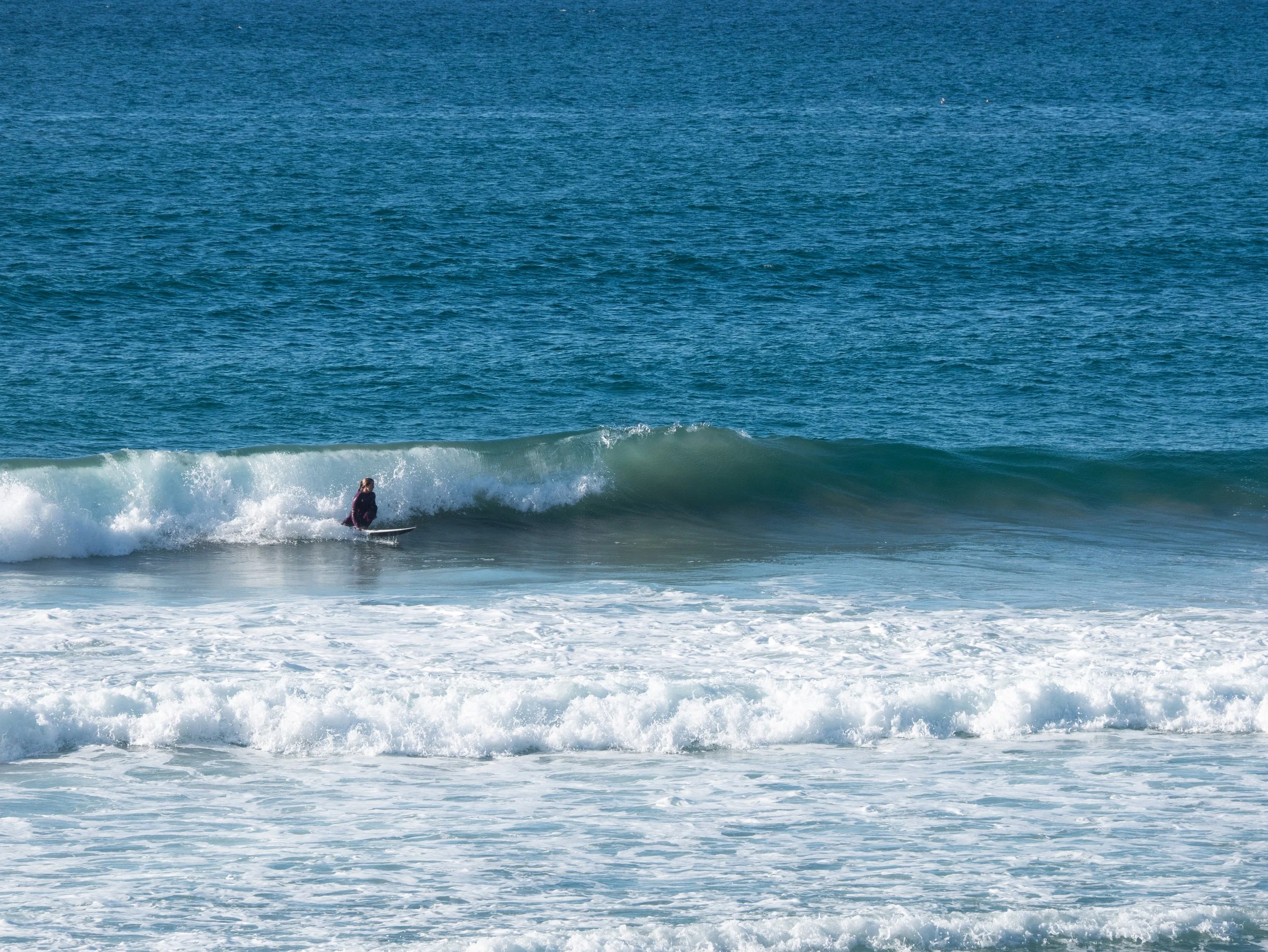 A person surfing on a wave at the beach with the ocean in the background.