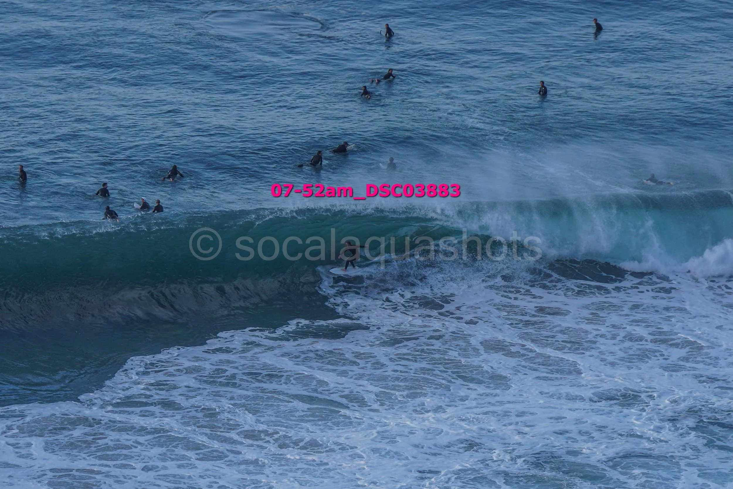 People swimming and surfing in the ocean with waves, some surfers riding a wave, others floating or swimming closer to the shore.