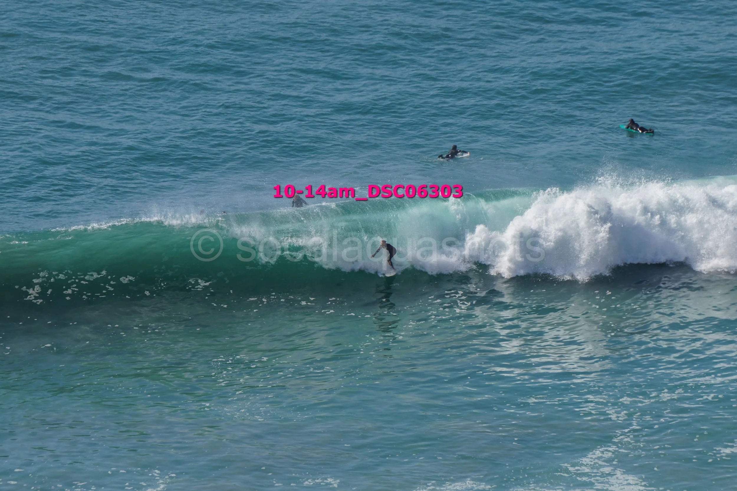 Surfer riding a wave in the ocean with three other surfers in the water nearby.
