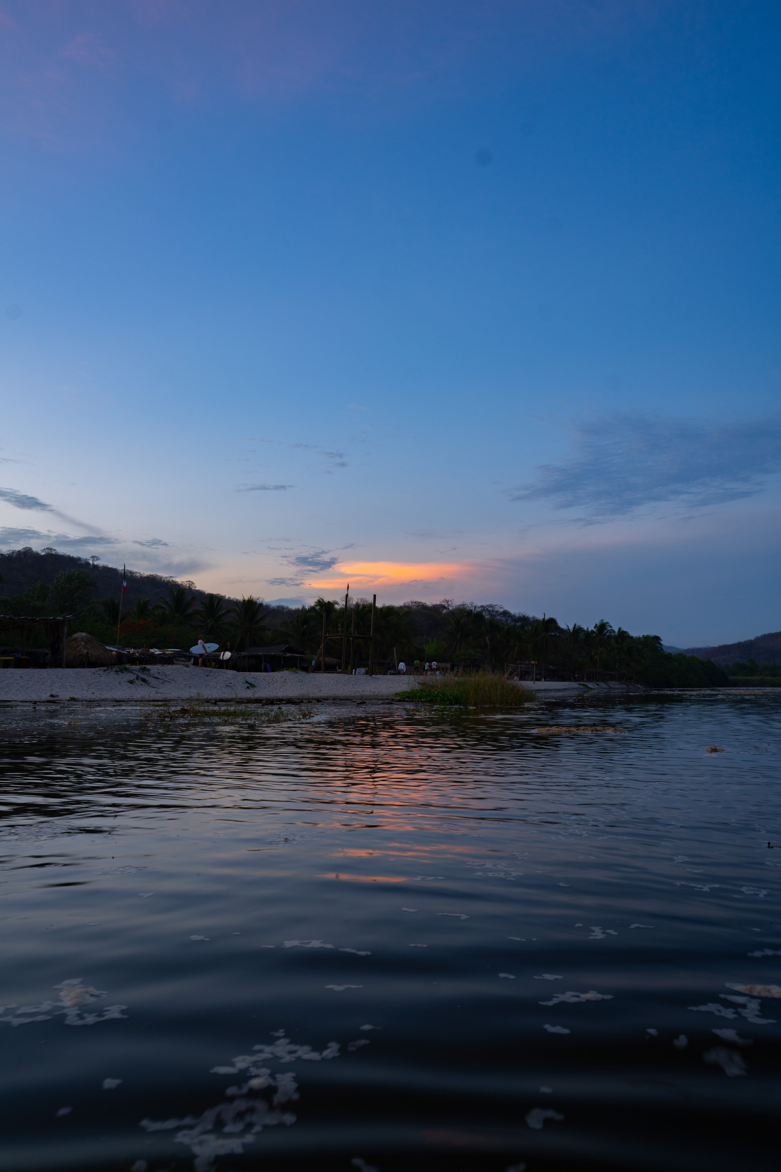 Sunset over a river with trees and a small village in the distance.