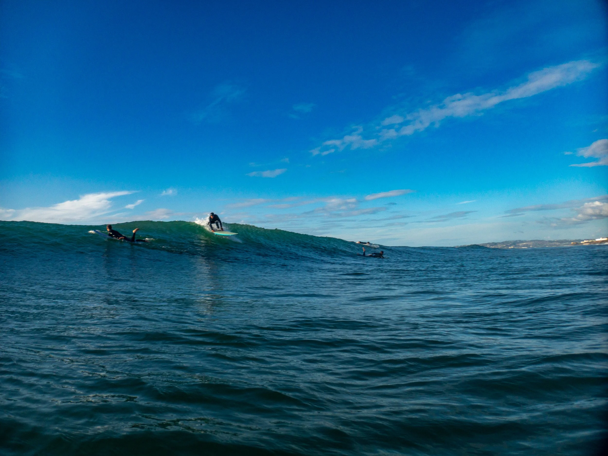 People surfing and paddleboarding in the ocean on a sunny day with blue sky and scattered clouds.
