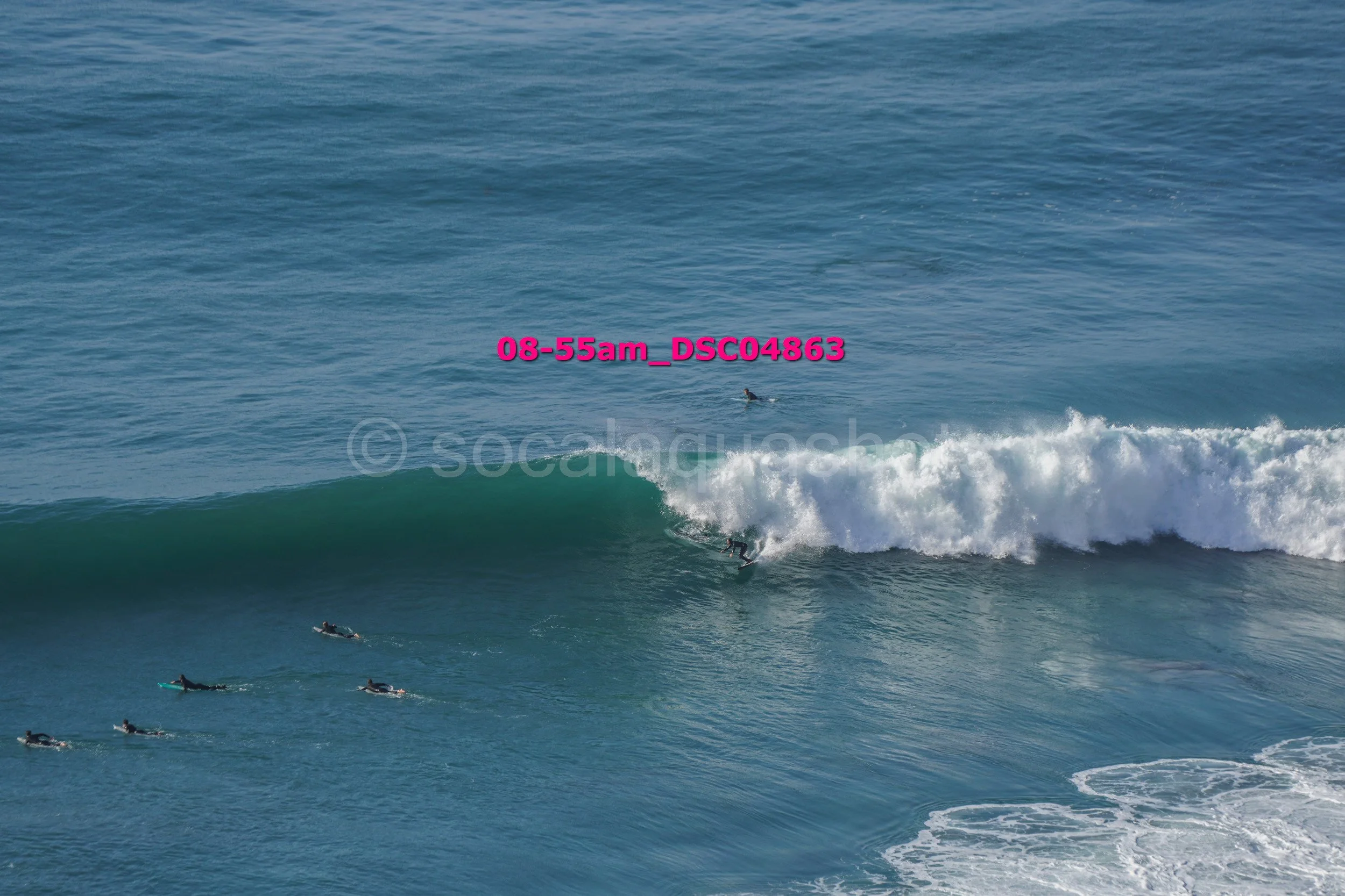 Surfer riding a wave in the ocean with several other surfers paddling nearby.