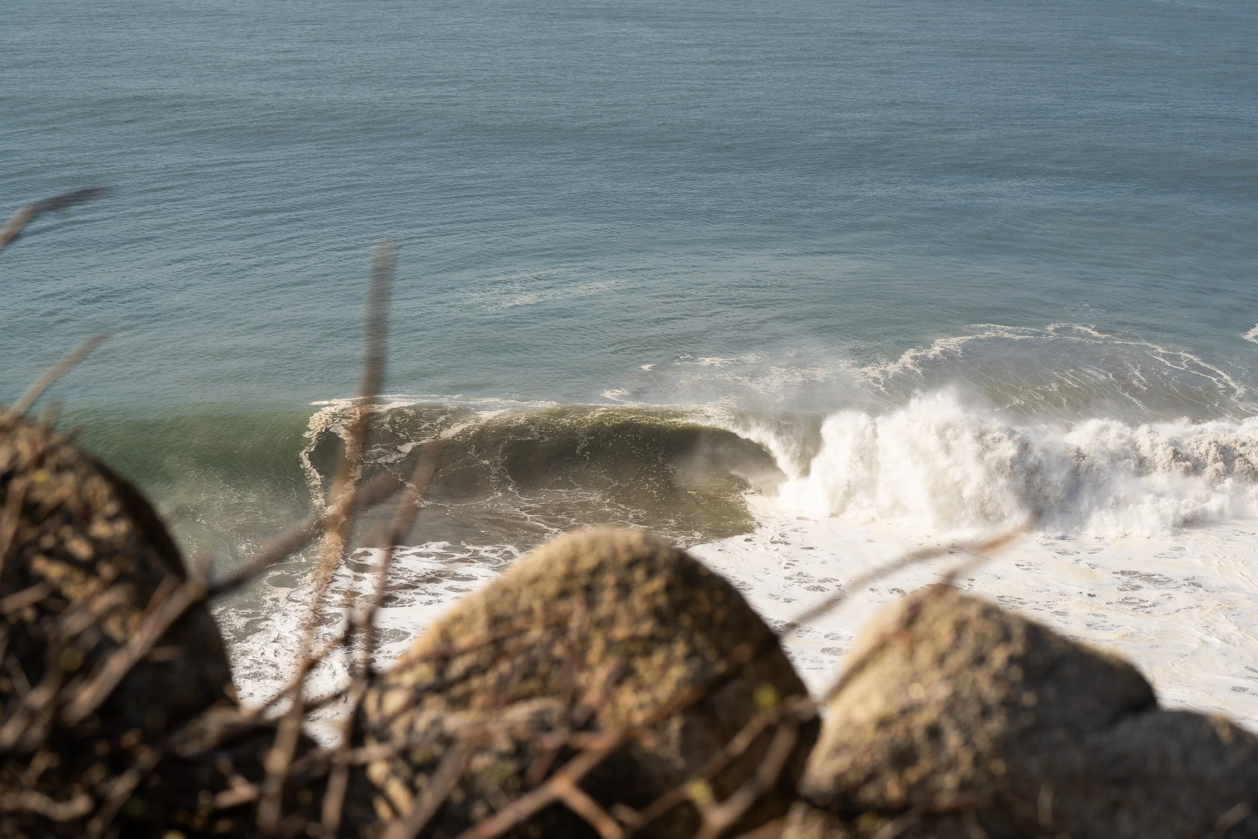 Rocks in the foreground with ocean waves crashing against the shoreline in the background.