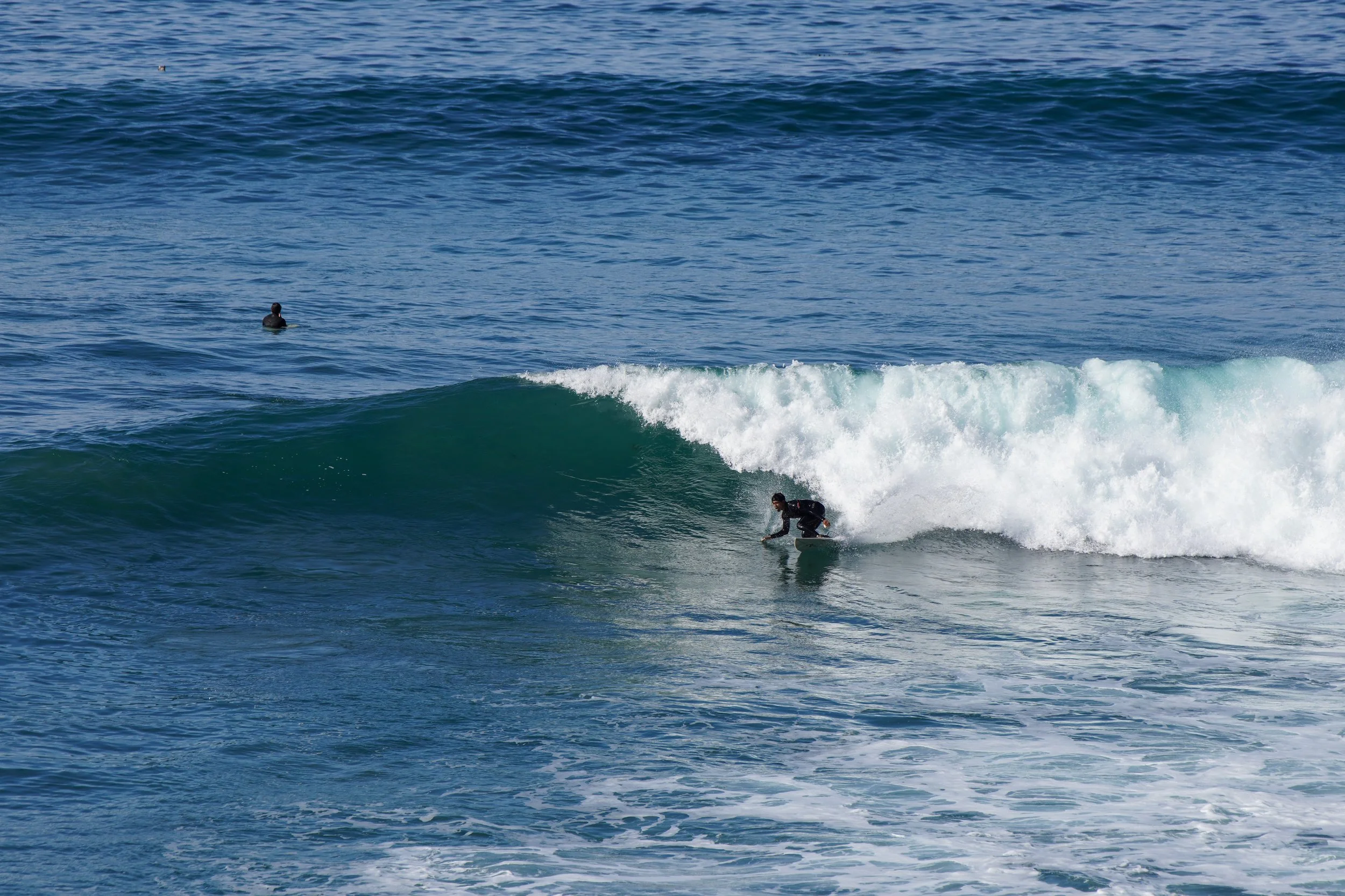 A person riding a surfboard on a wave in the ocean with another surfer in the background.