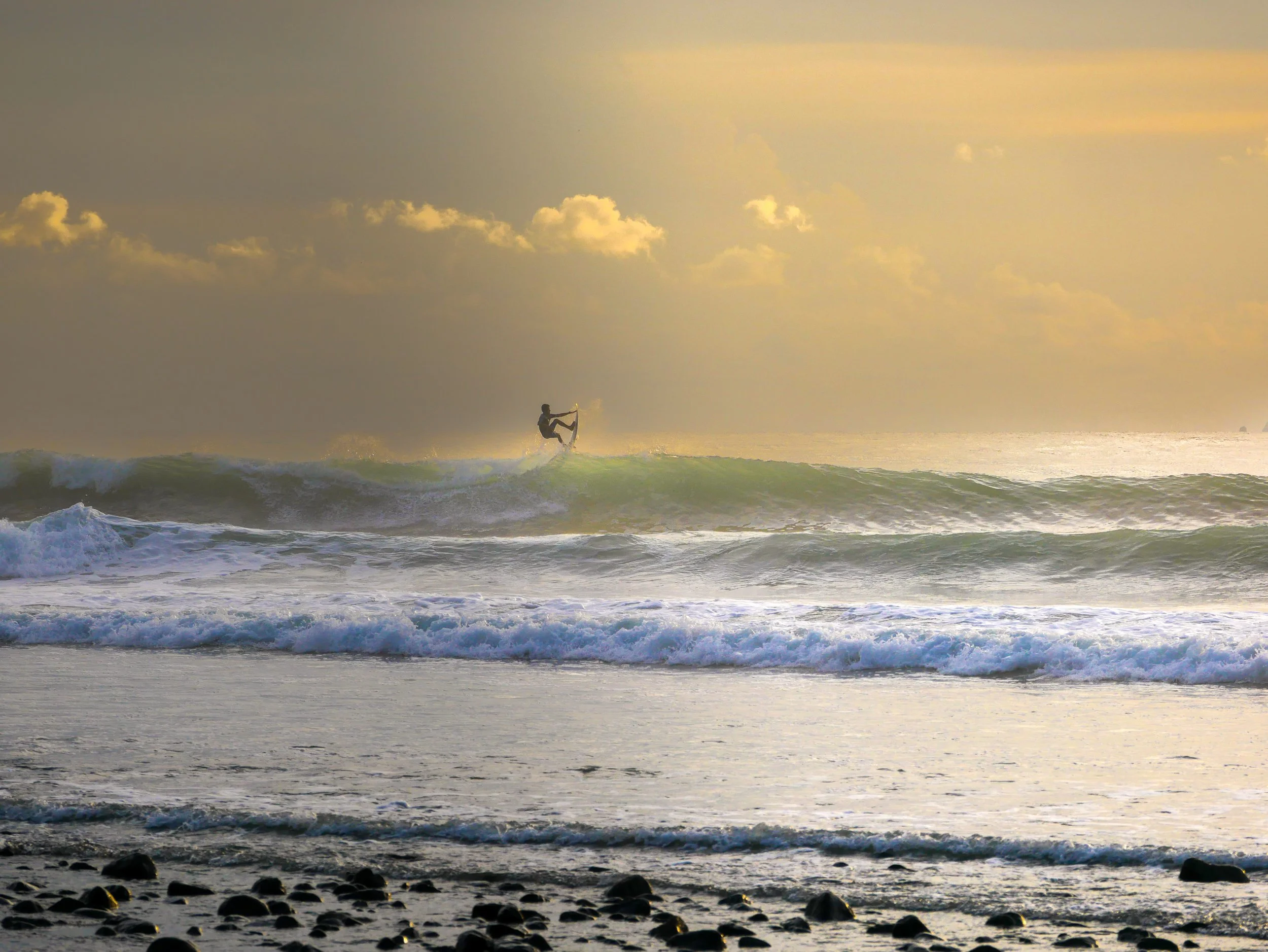 Surfer catching air on ocean wave at sunset with rocky shore in foreground