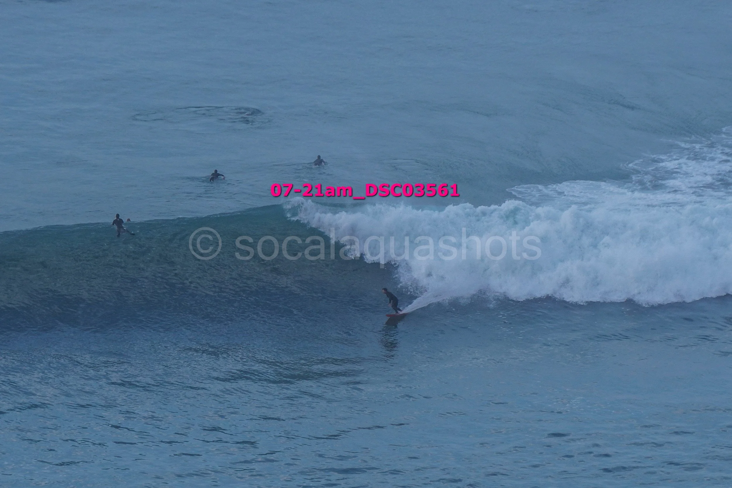 A surfer riding a wave with several people swimming in the water nearby.