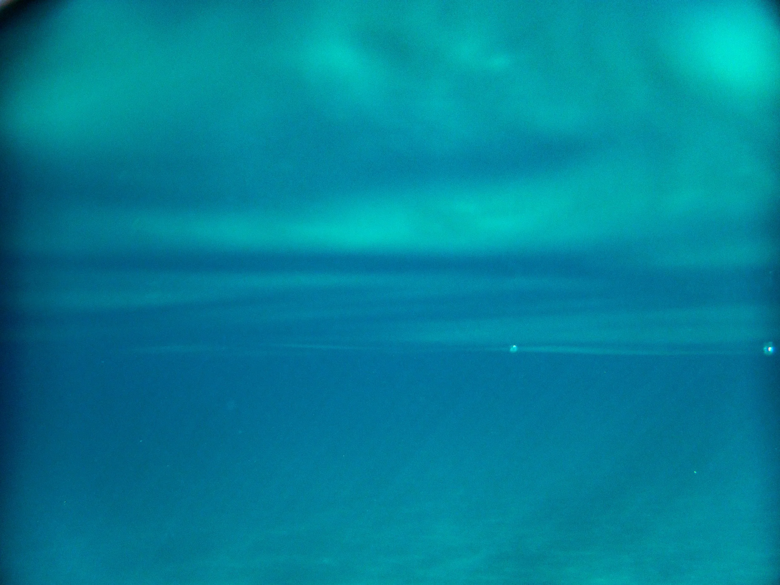 Bright turquoise and blue light beams shining through a dark sky, with some small points of light visible in the distance.