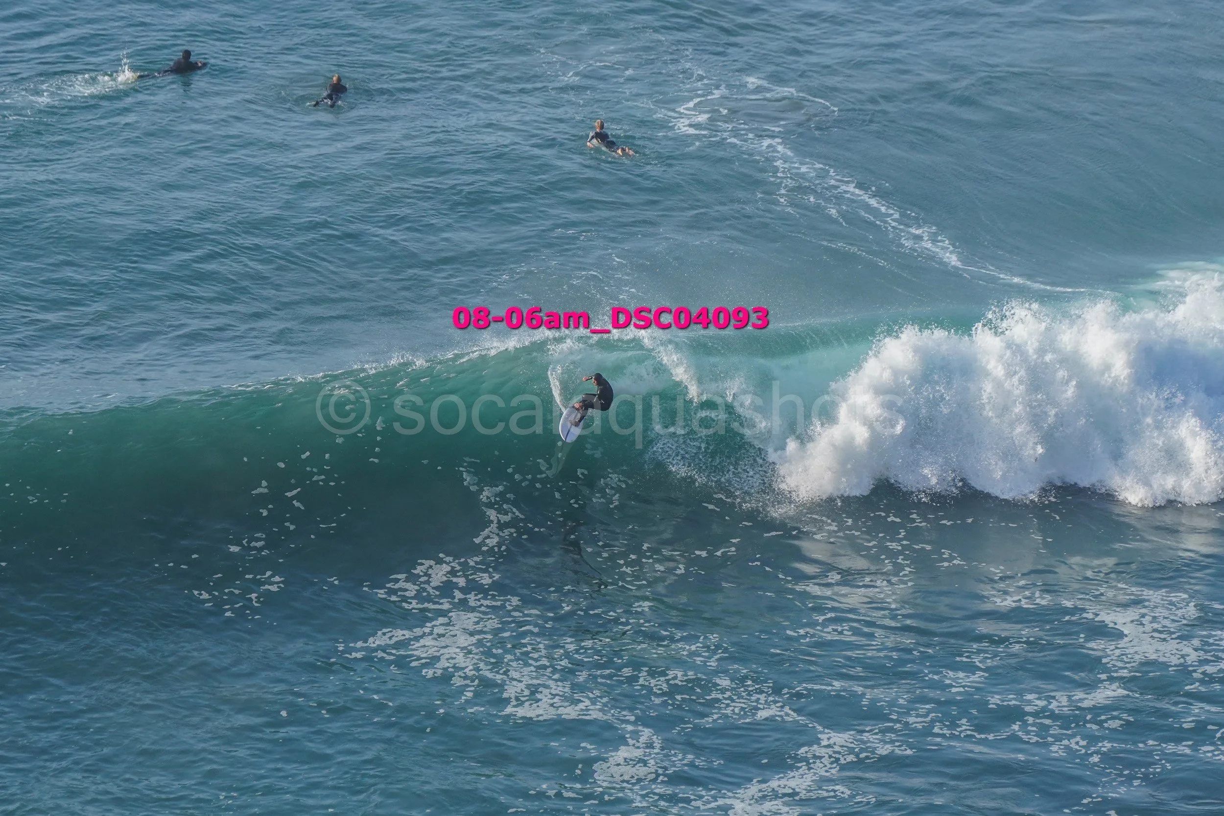 A person surfing on a large wave with three other surfers in the water nearby.