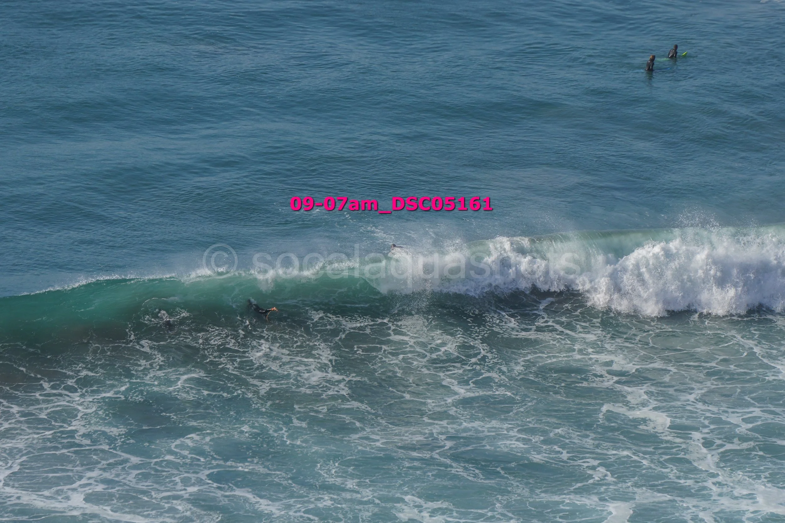 Surfers in wetsuits riding and waiting for waves in the ocean.