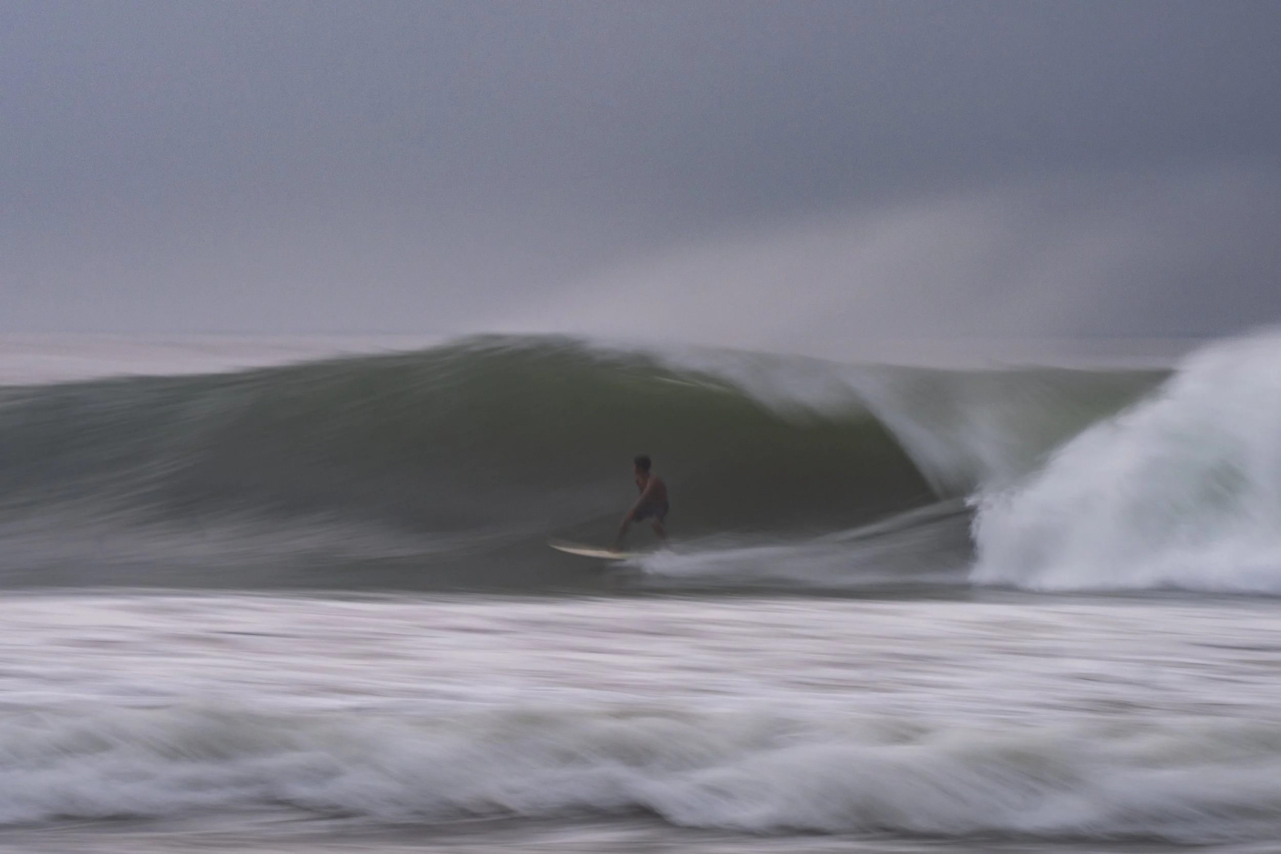 Someone surfing on a wave in the ocean during cloudy weather.