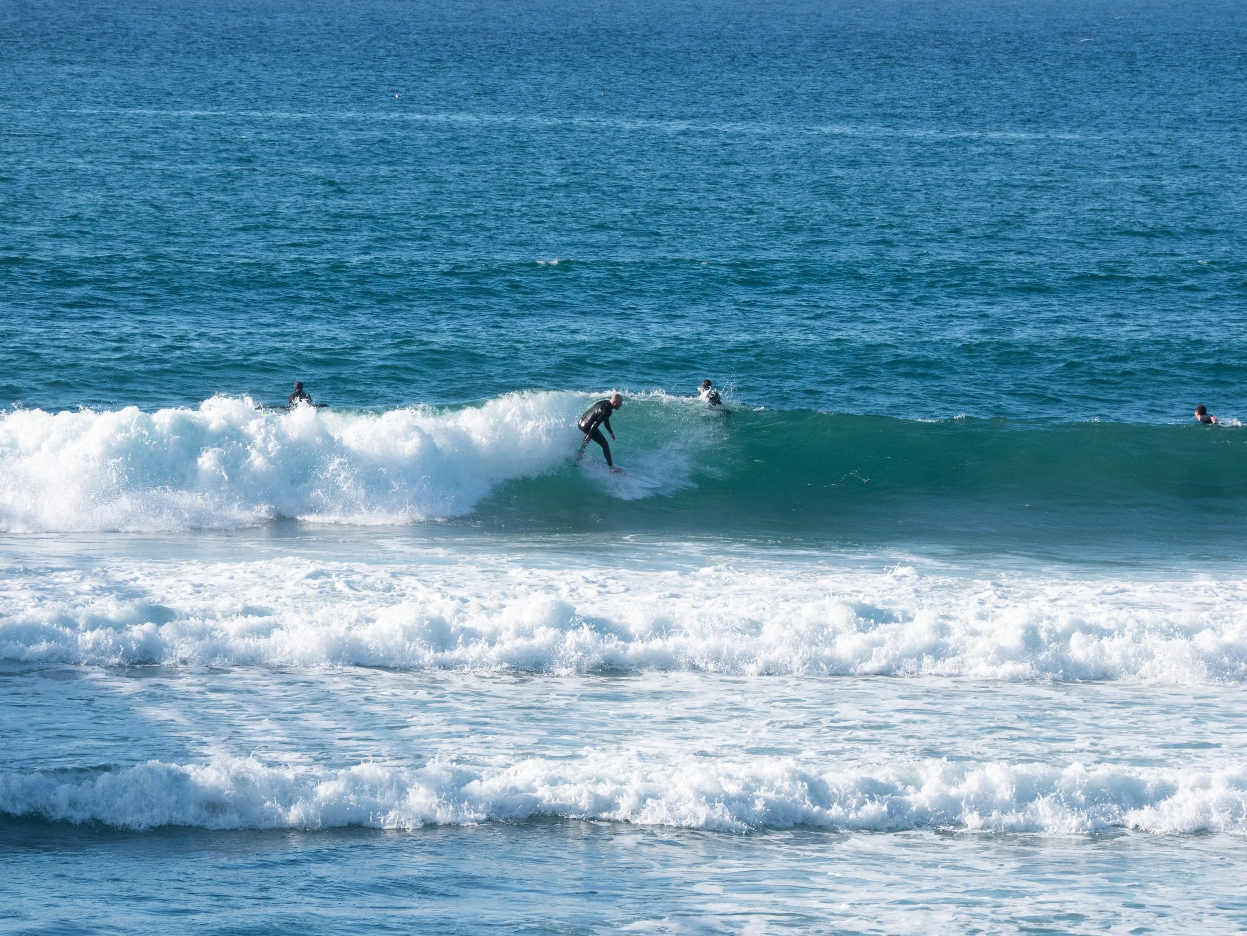 A person surfing on a wave at the beach with three other surfers paddling nearby.