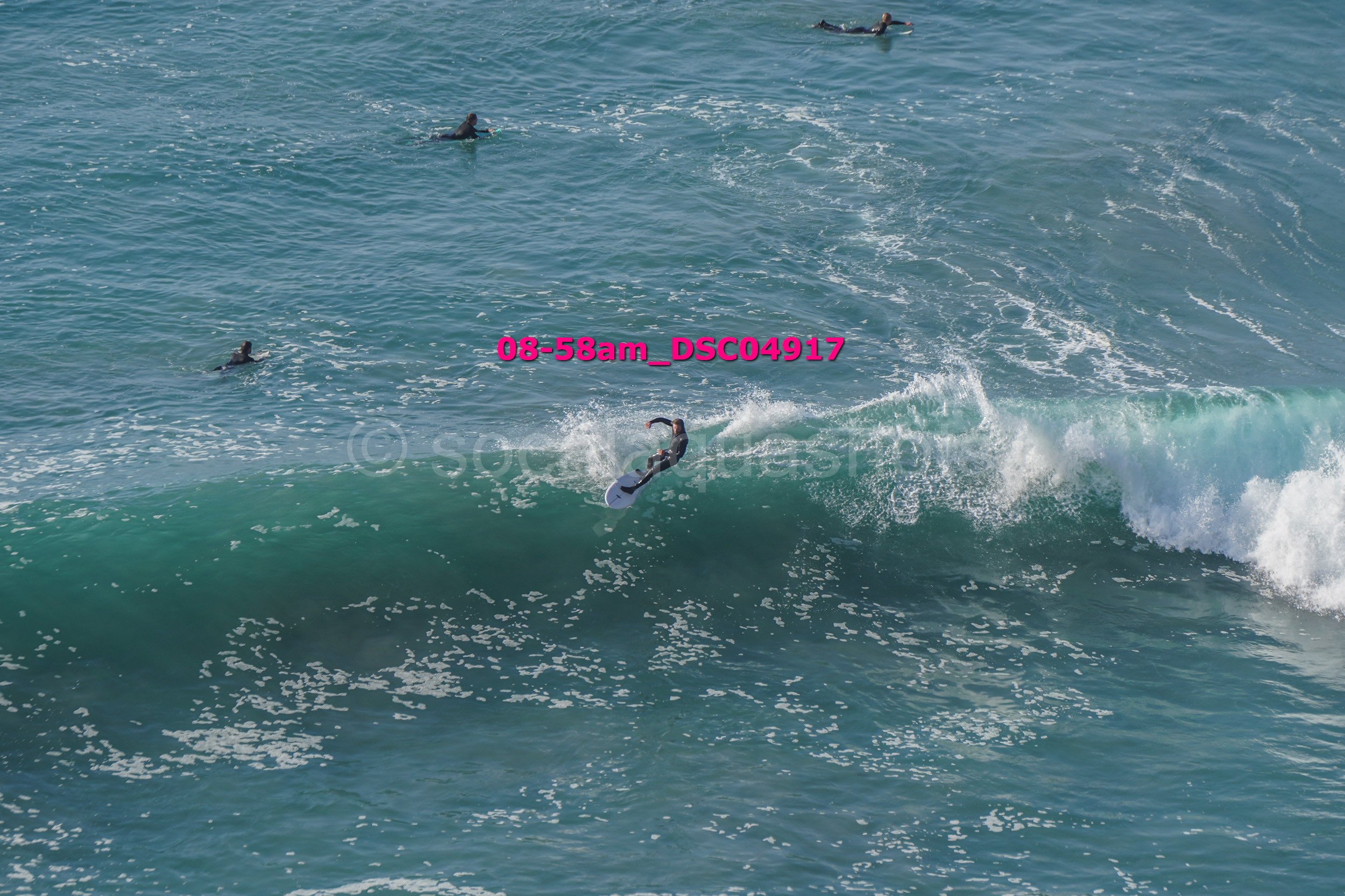 A person surfing on a wave with several surfers in the water nearby.