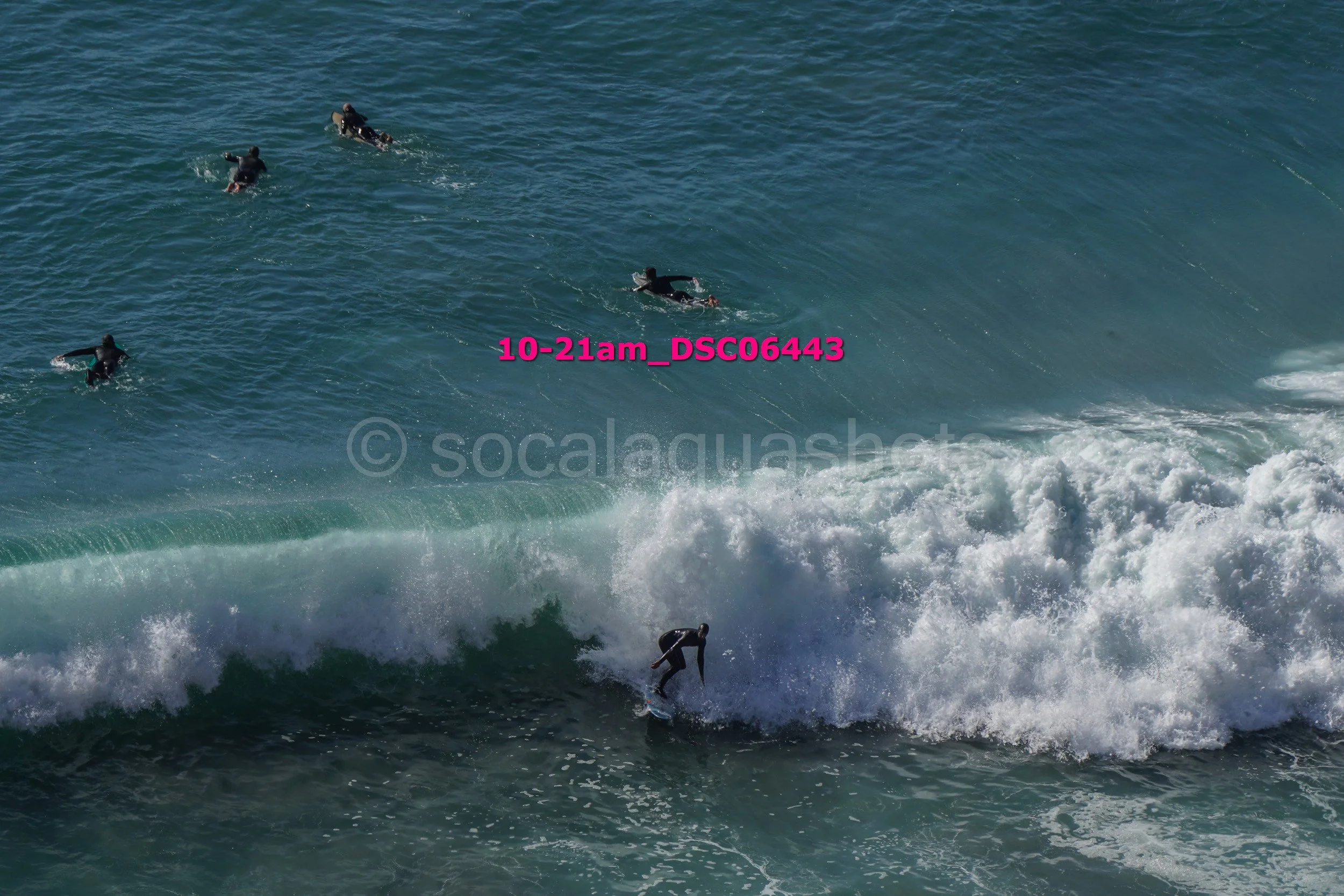 Surfer riding a wave with three surfers in the water behind him.