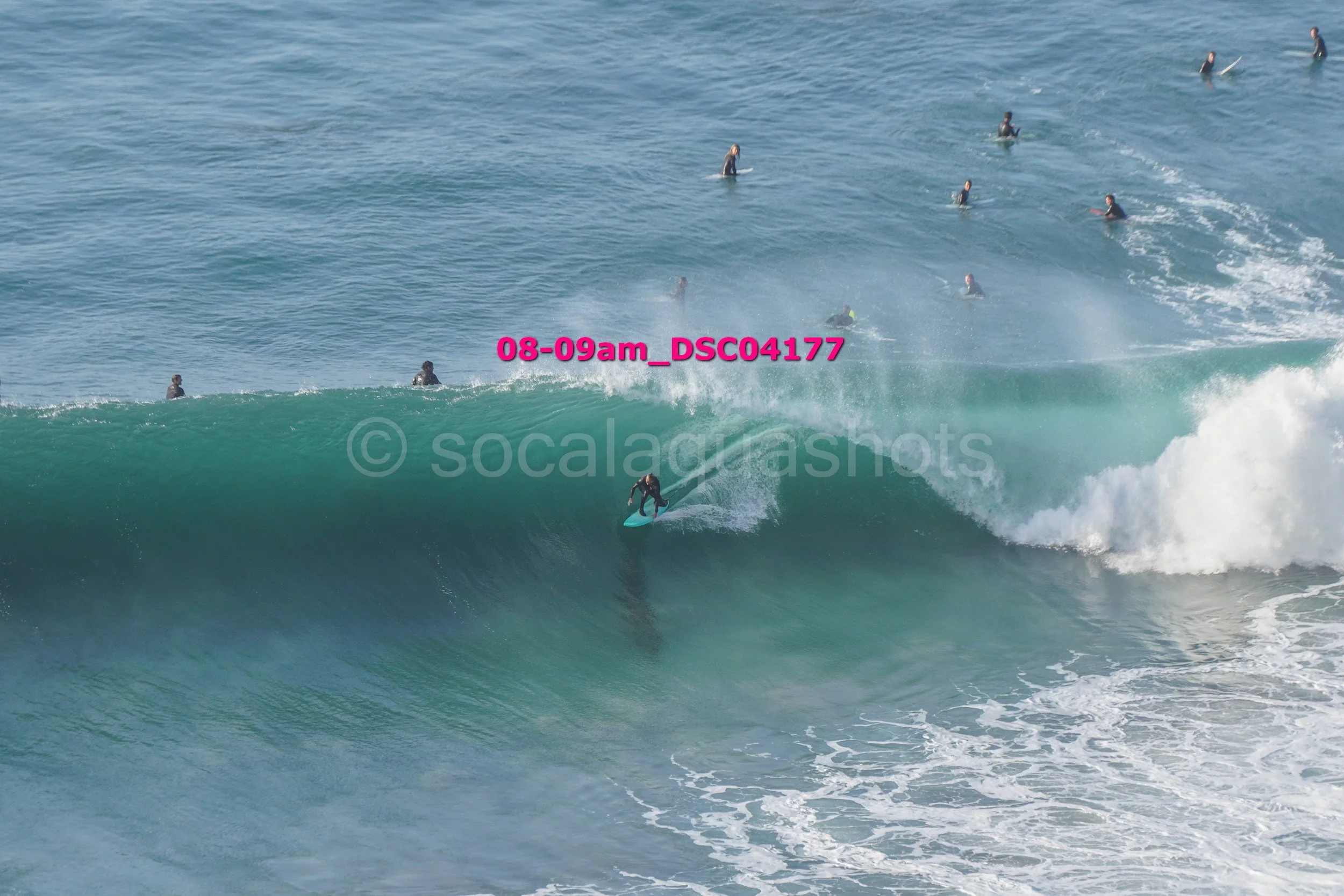 A surfer riding a large wave with several people in the water and on surfboards in the background.
