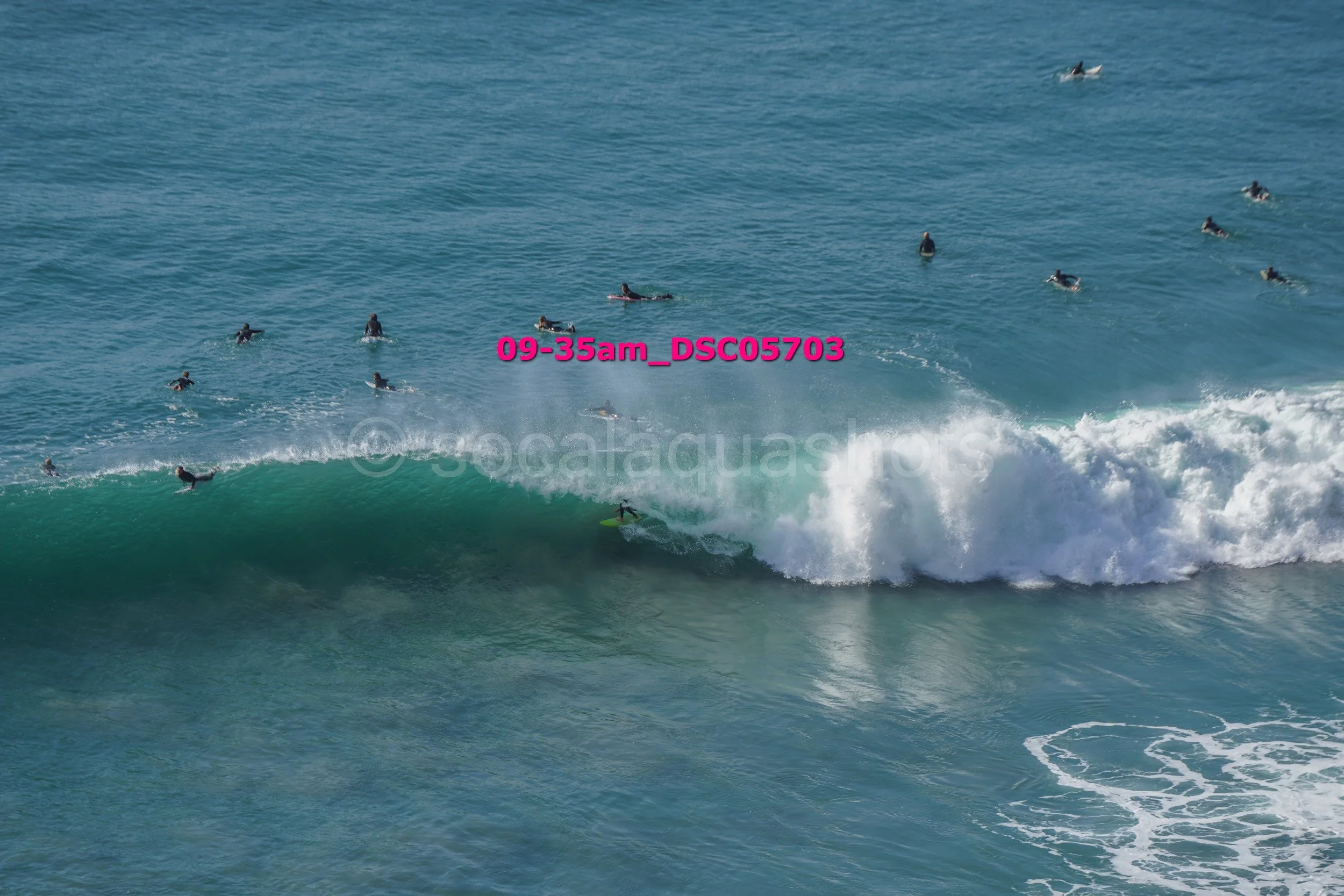 A large group of surfers in the ocean, some riding a wave while others wait in the water.