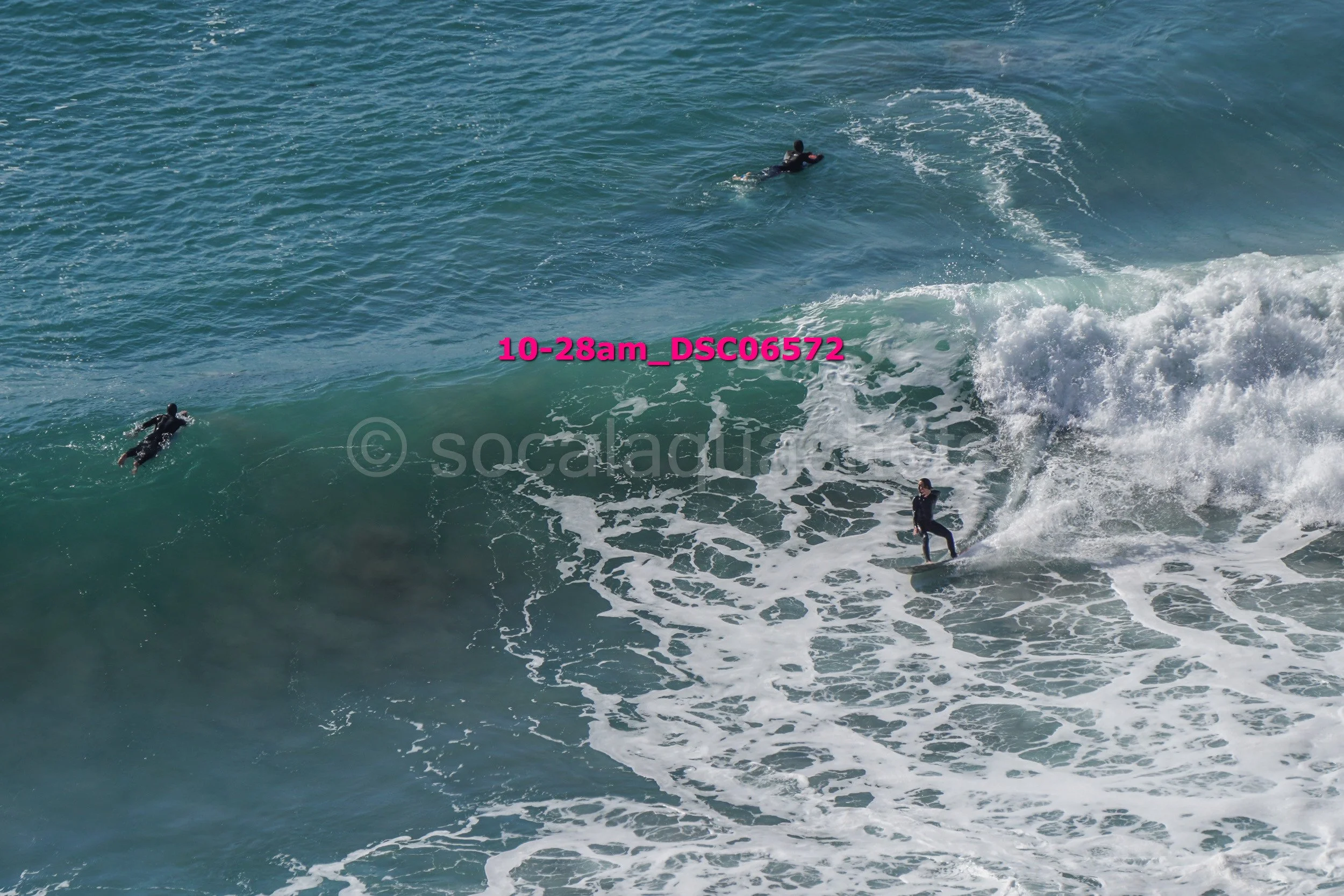 Three surfers riding and paddling on ocean waves with a shoreline visible in the distance.