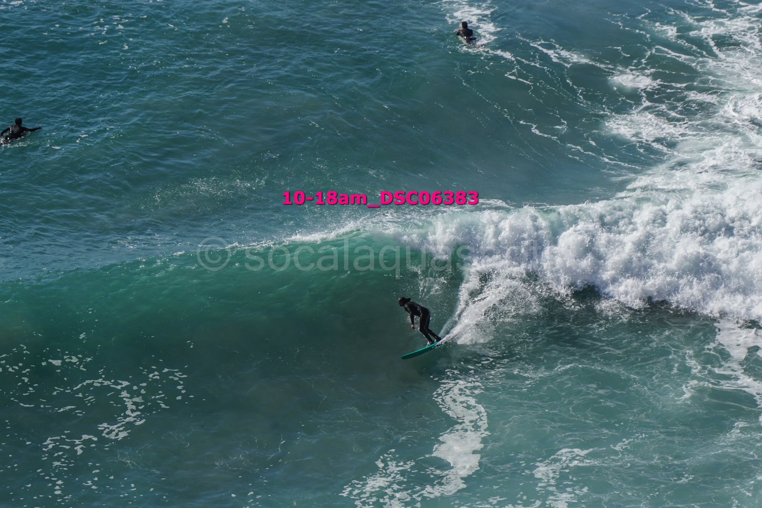 Surfer riding a wave in the ocean, with other surfers visible in the background.