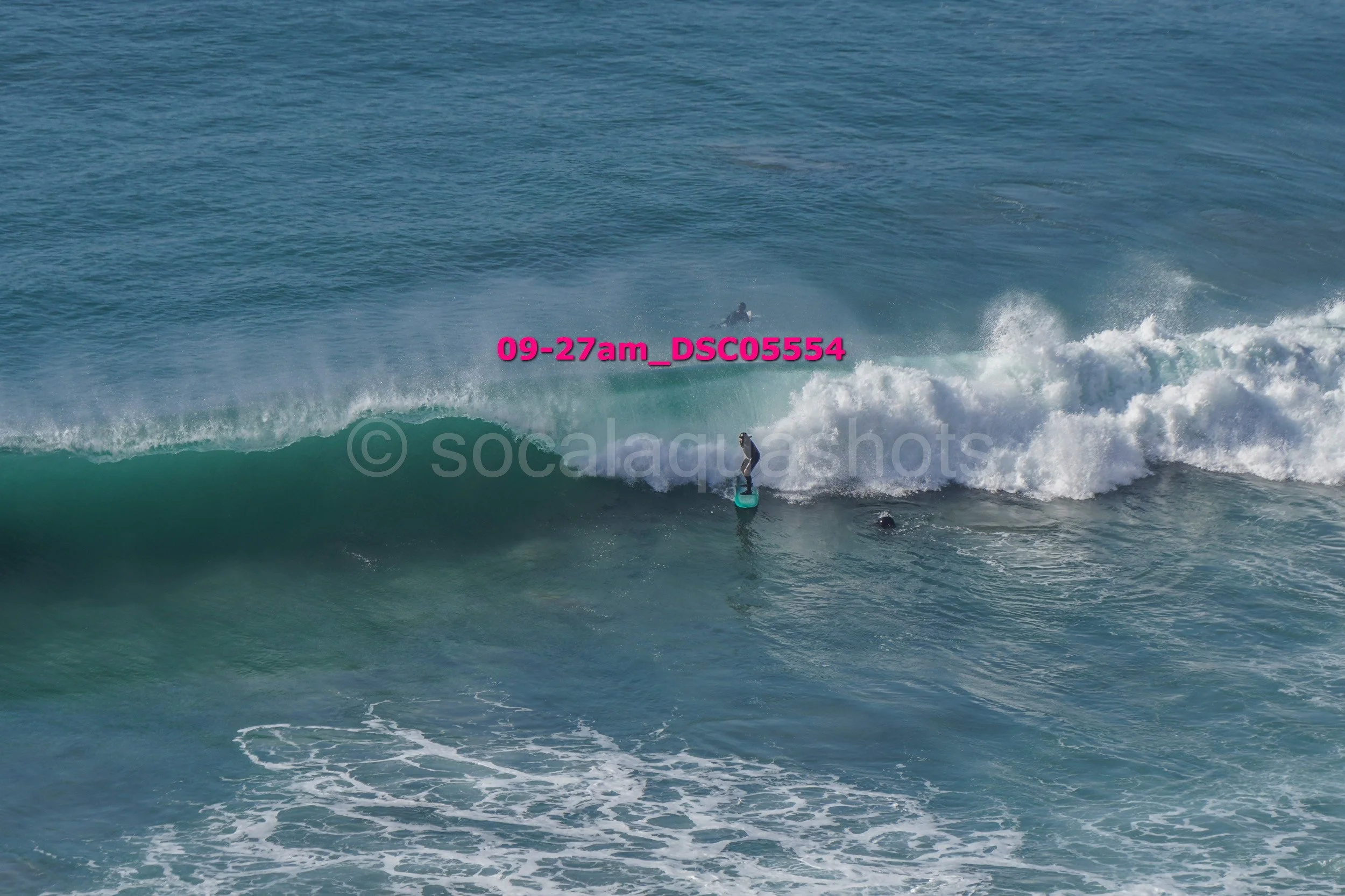Surfer riding a wave in the ocean with a person swimming nearby and a jet ski in the background.