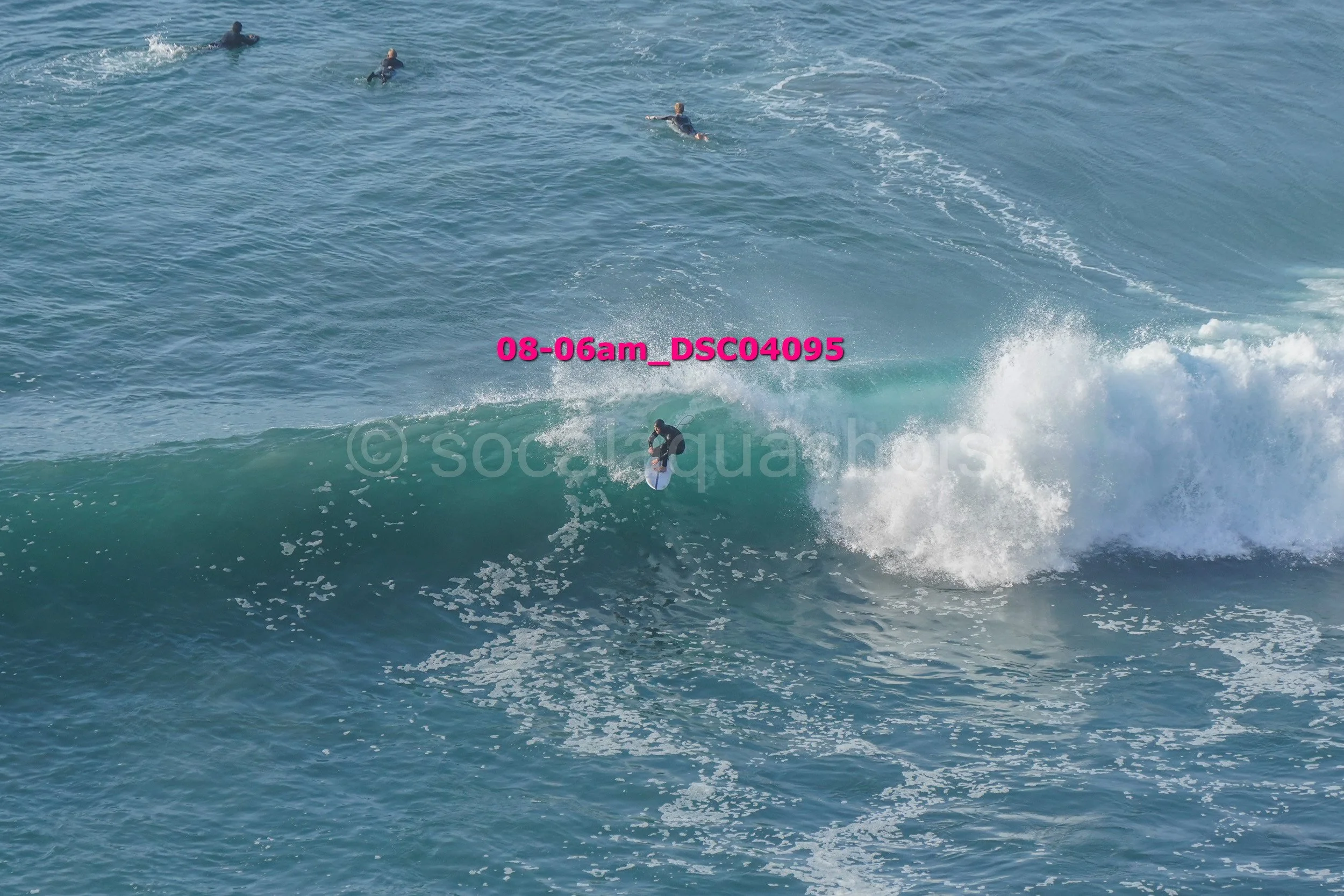 A person surfing on a wave in the ocean, with several other surfers visible in the background.