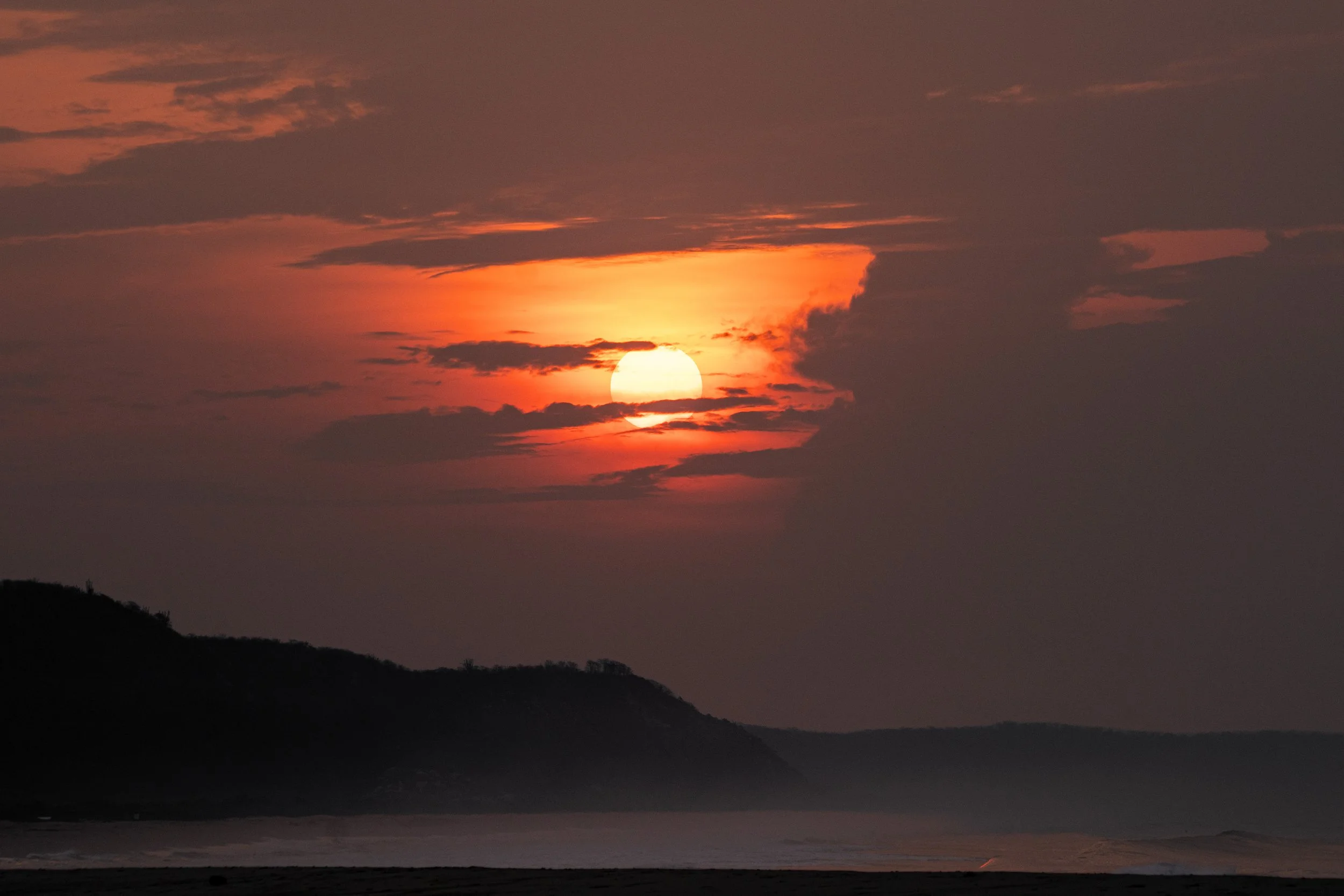 Sunset over a landscape with mountains and cloudy sky.