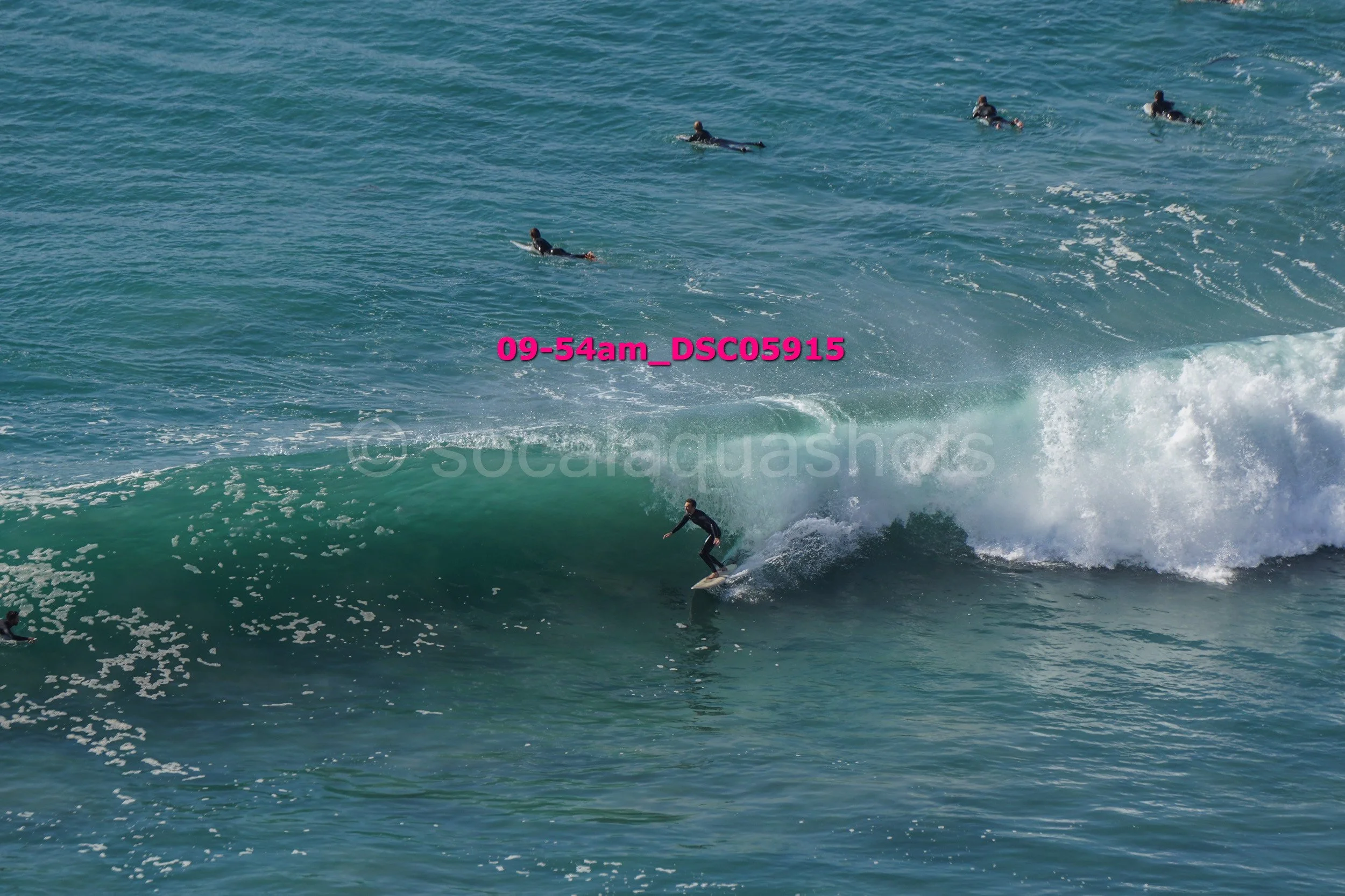 Surfer riding a wave with multiple spectators in the water watching.