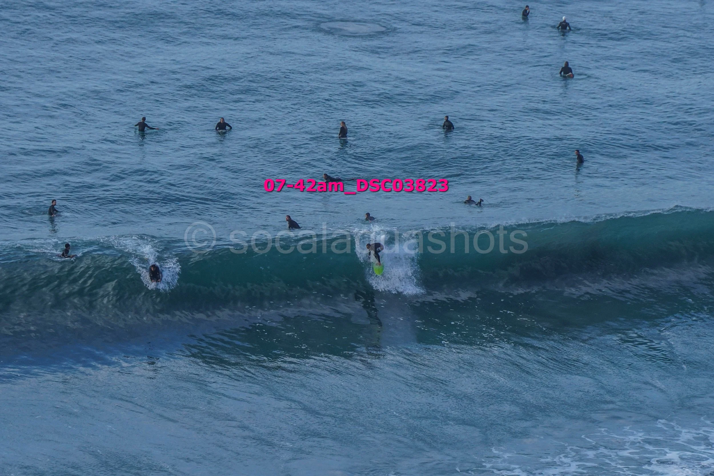 Surfer riding a wave with many surfers in the water around him.