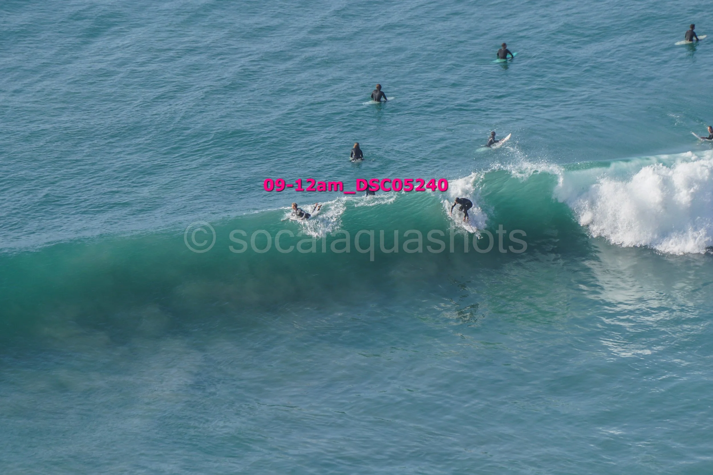 Several surfers riding waves and others waiting in the ocean water during daytime.
