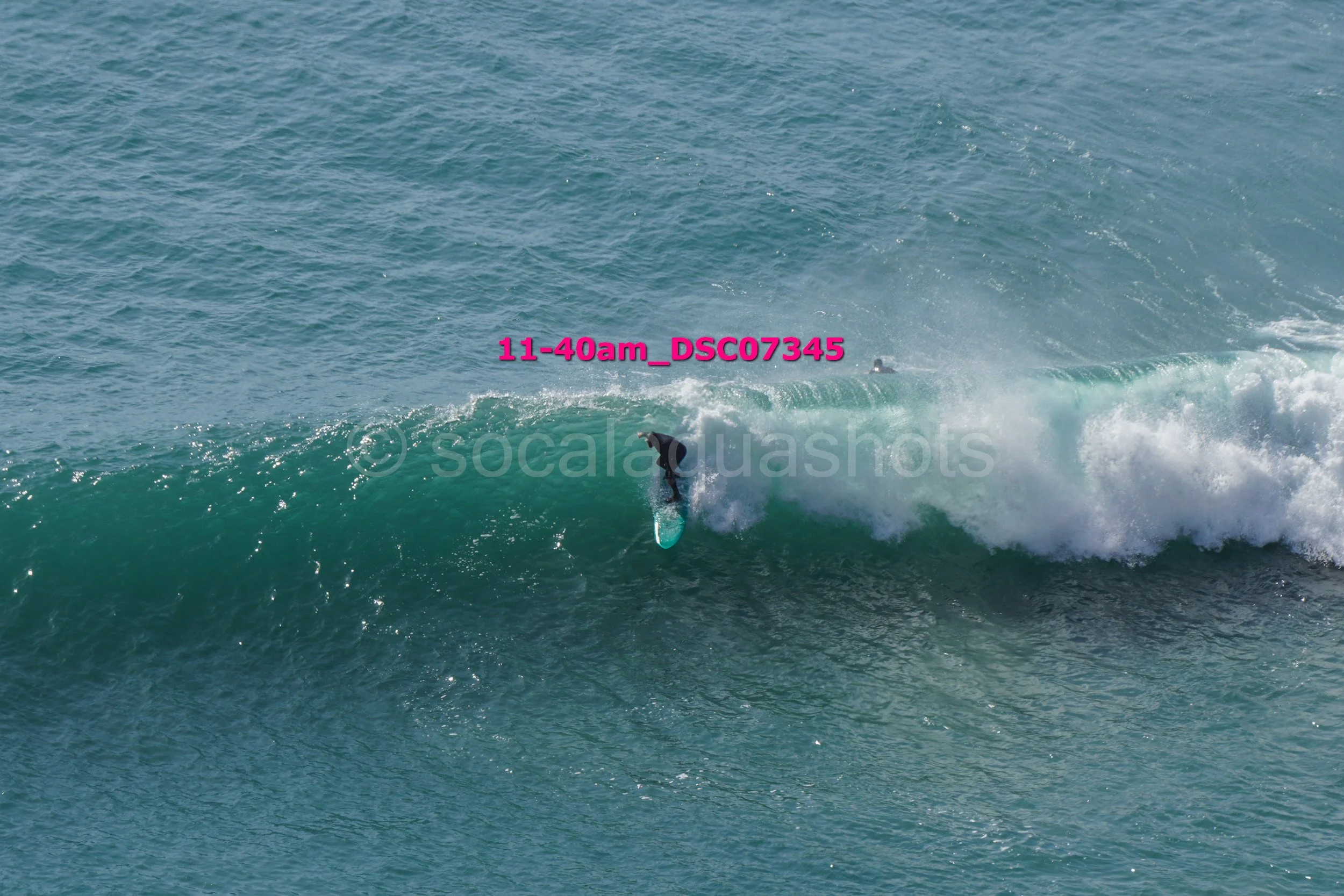 A surfer riding a wave in the ocean with water splashing around, captured from a distance.