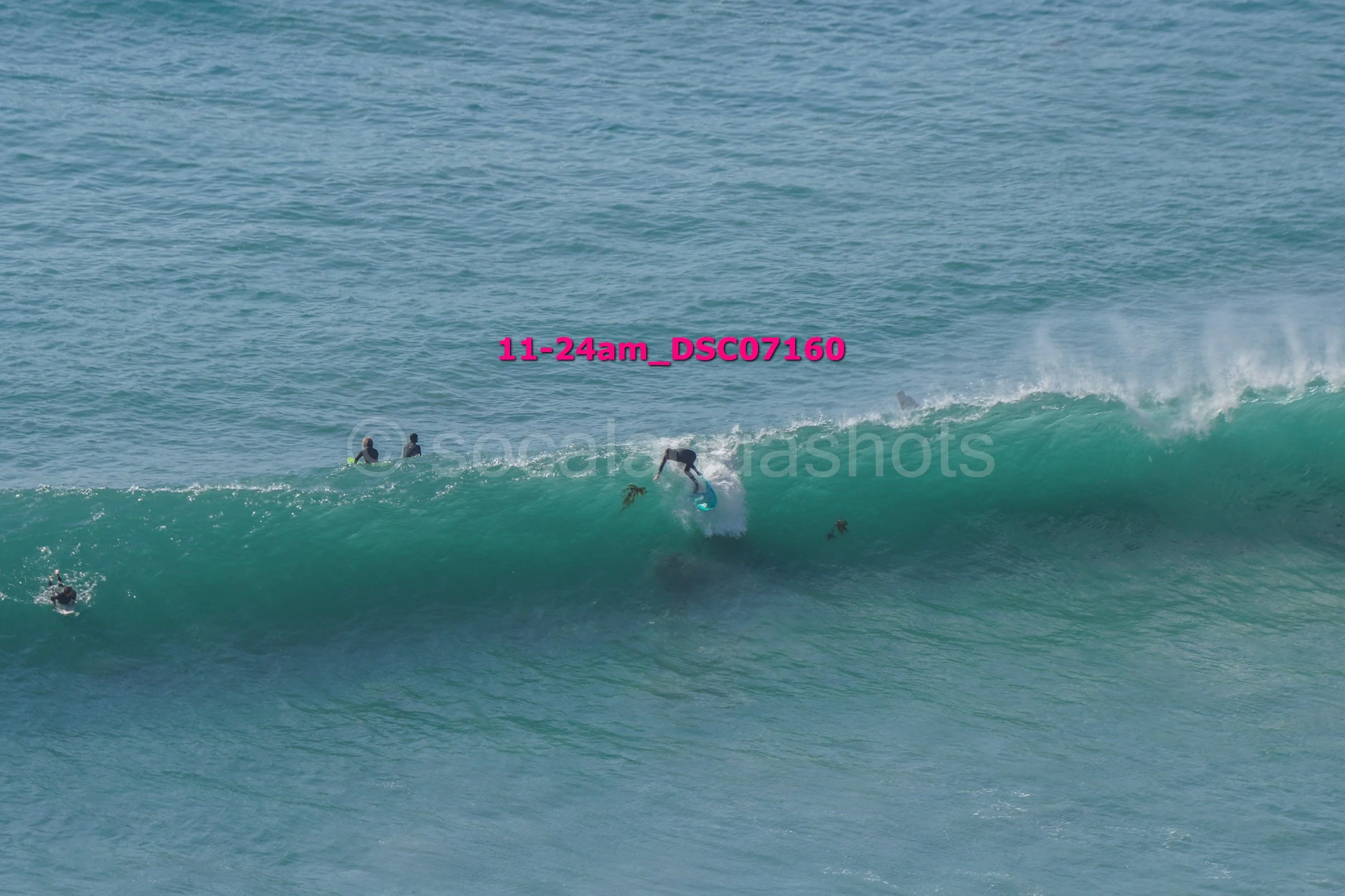 Surfer riding a large wave in the ocean with several other surfers in the water nearby.