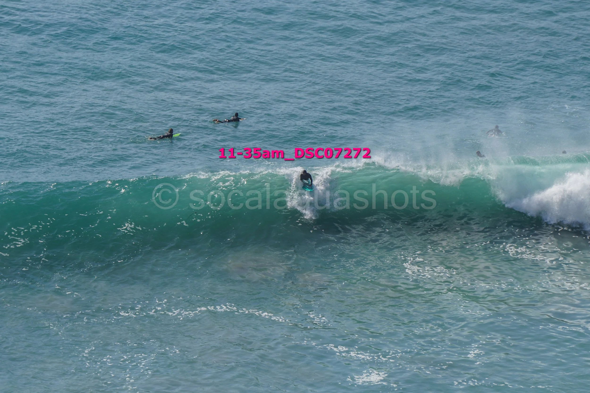 Surfer riding a wave with three people in the water watching, ocean scene during daytime.