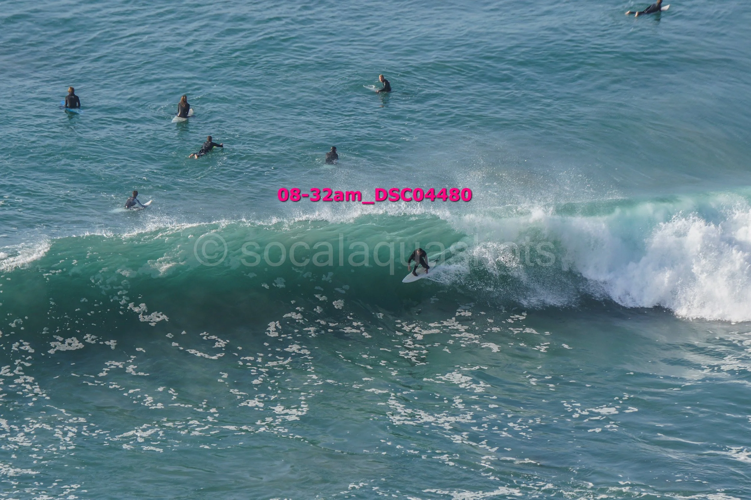 A person surfing on a wave with several other surfers in the water nearby.