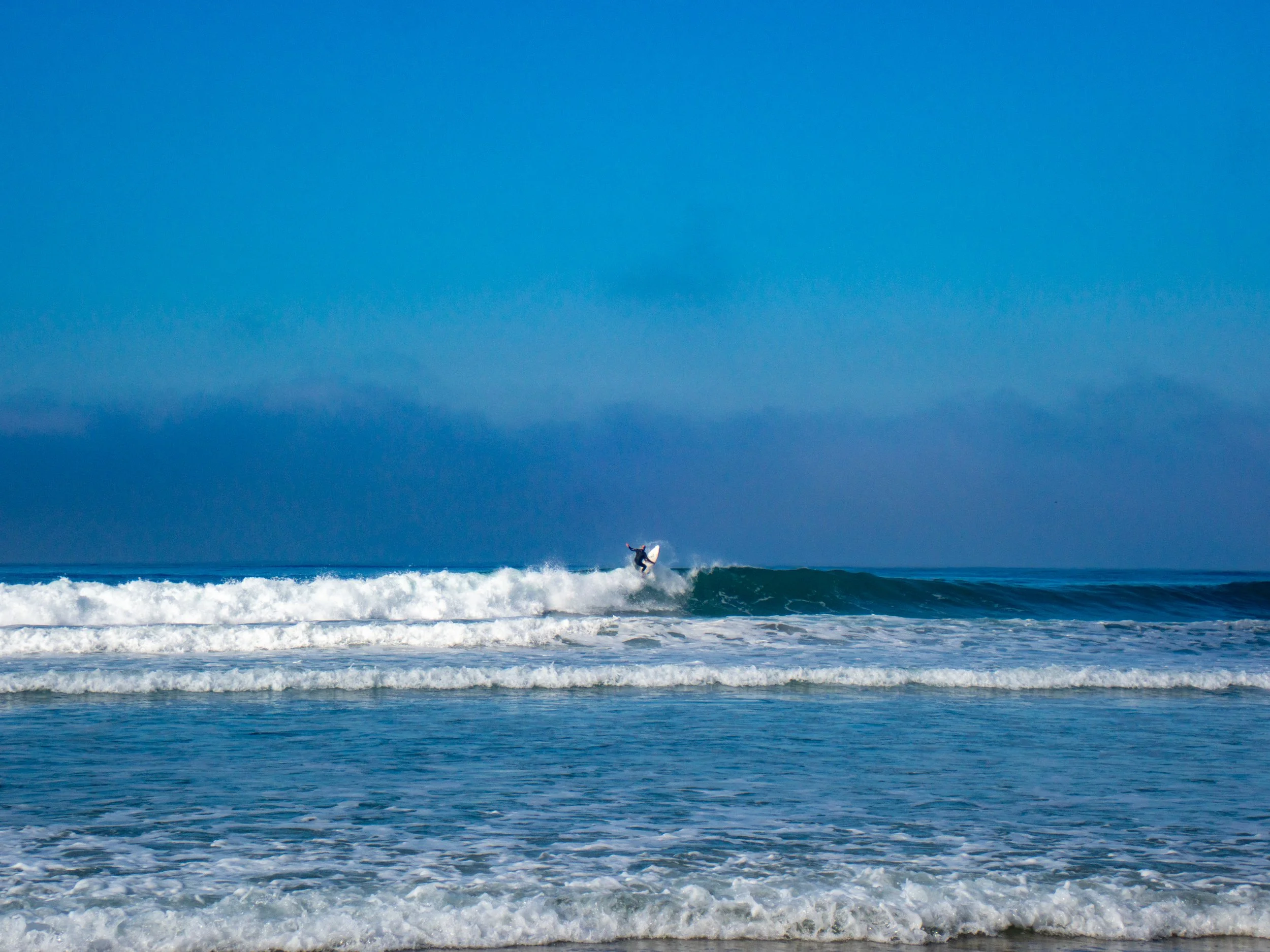 A surfer riding a wave at the beach with a clear blue sky in the background.