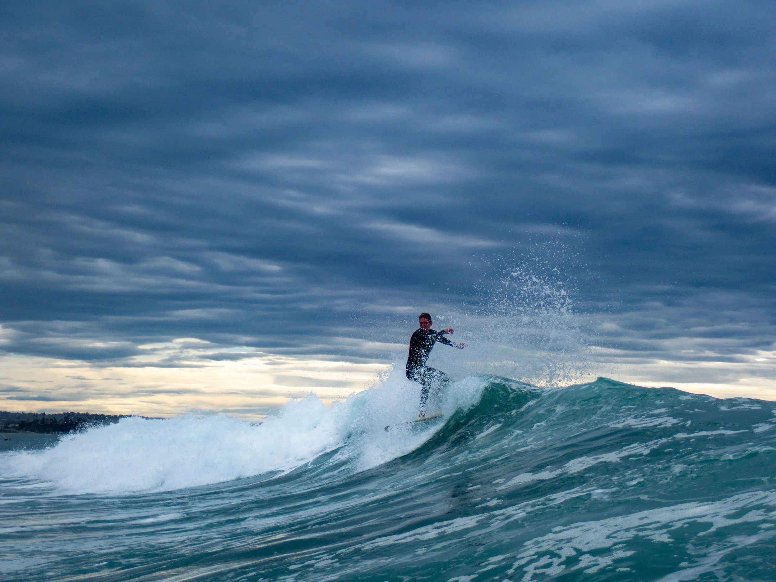 A person surfing on a wave under a cloudy sky.