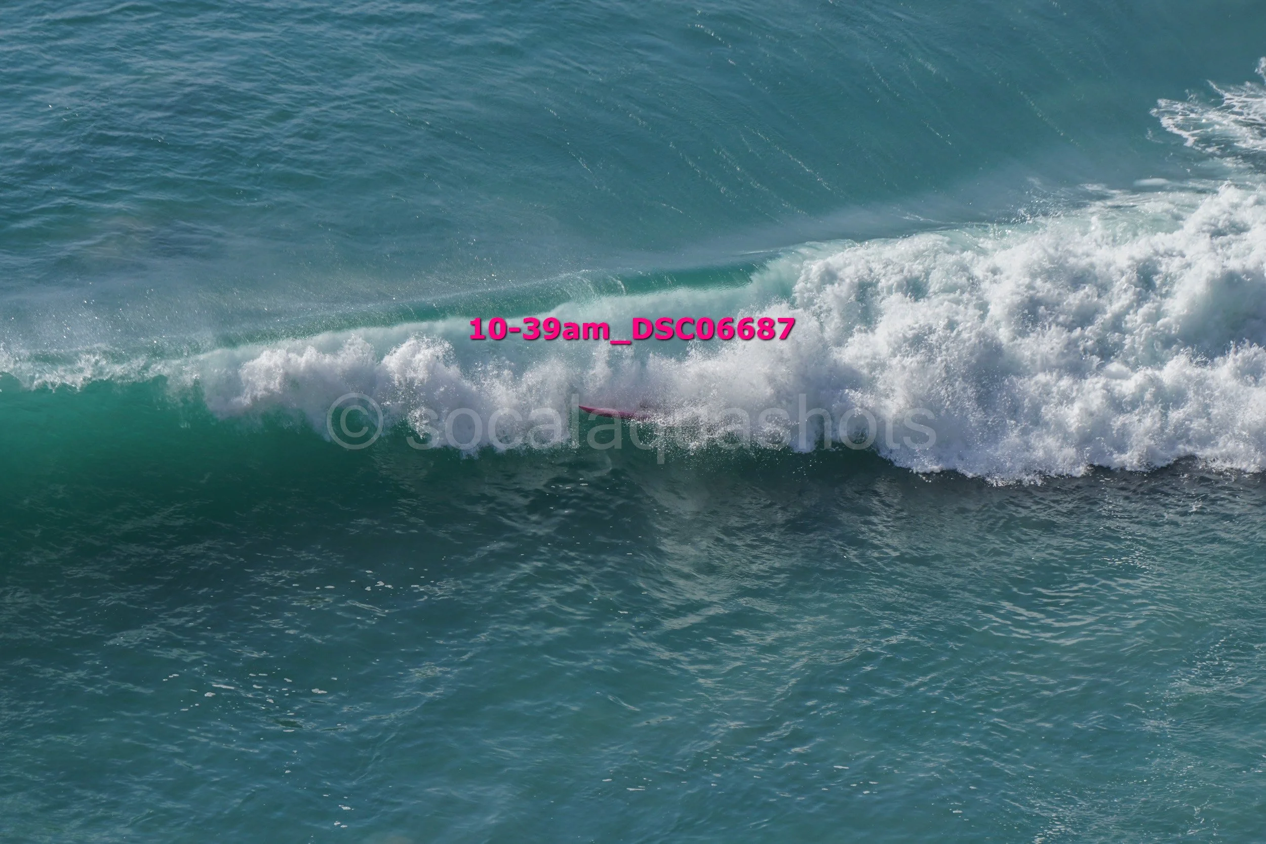 Ocean wave with a surfboard partially submerged in the water, seen from above.