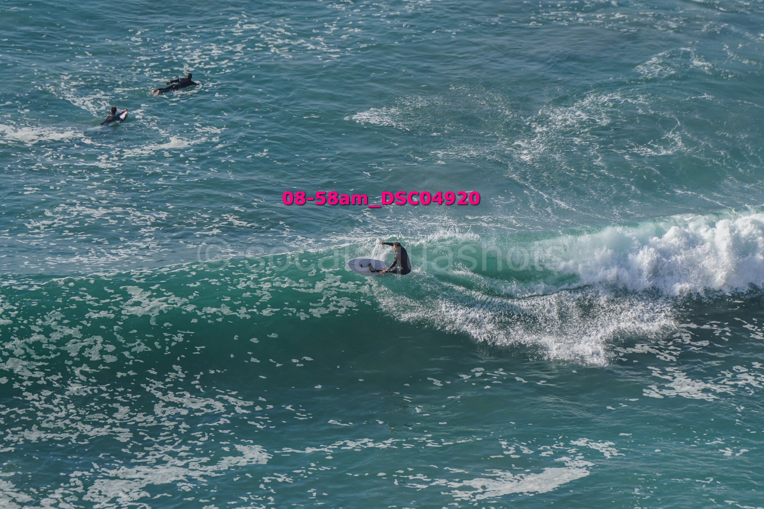 A person surfing on a wave with two other surfers in the water nearby in the ocean.