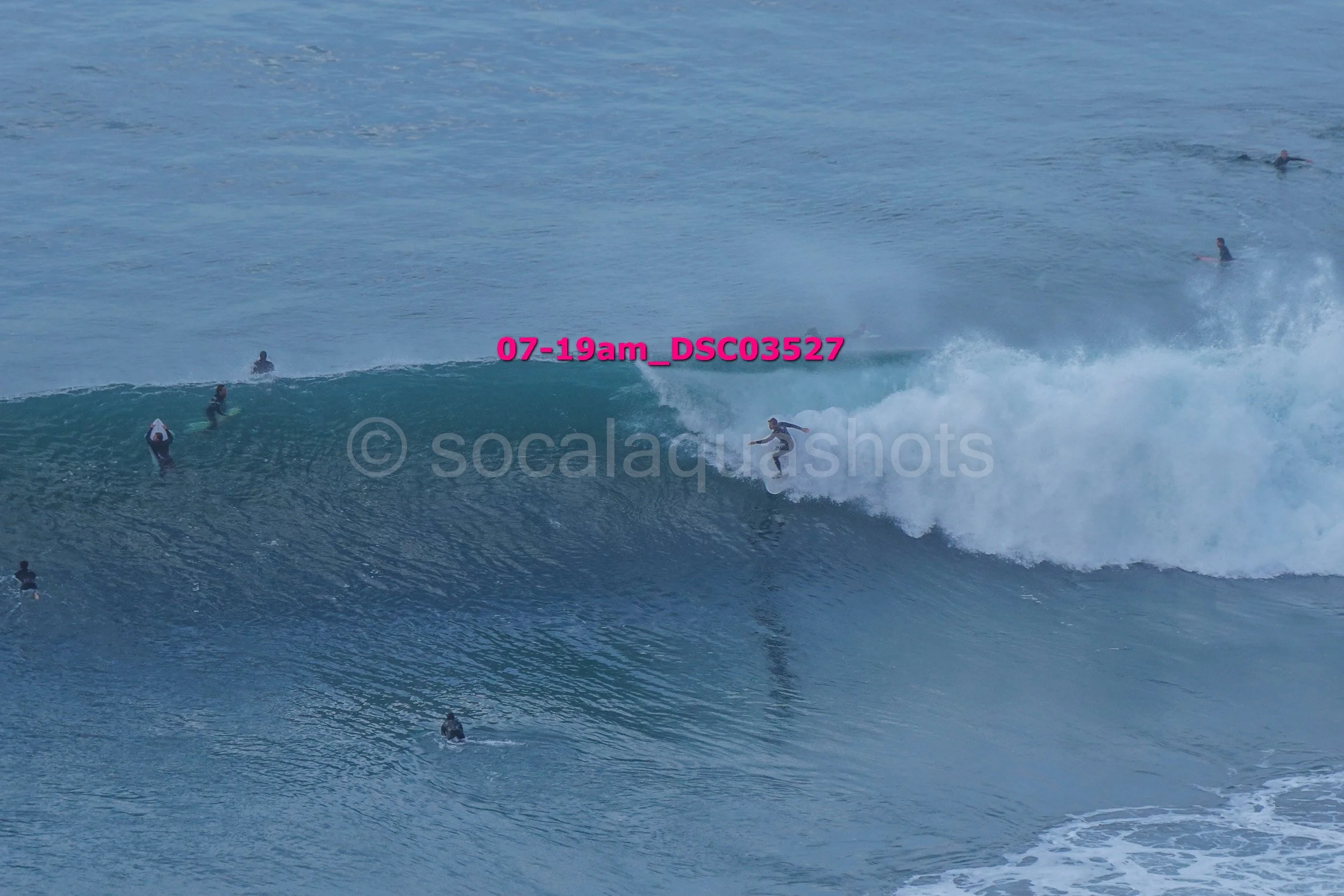 Surfer riding a wave with several surfers in the water in the background.