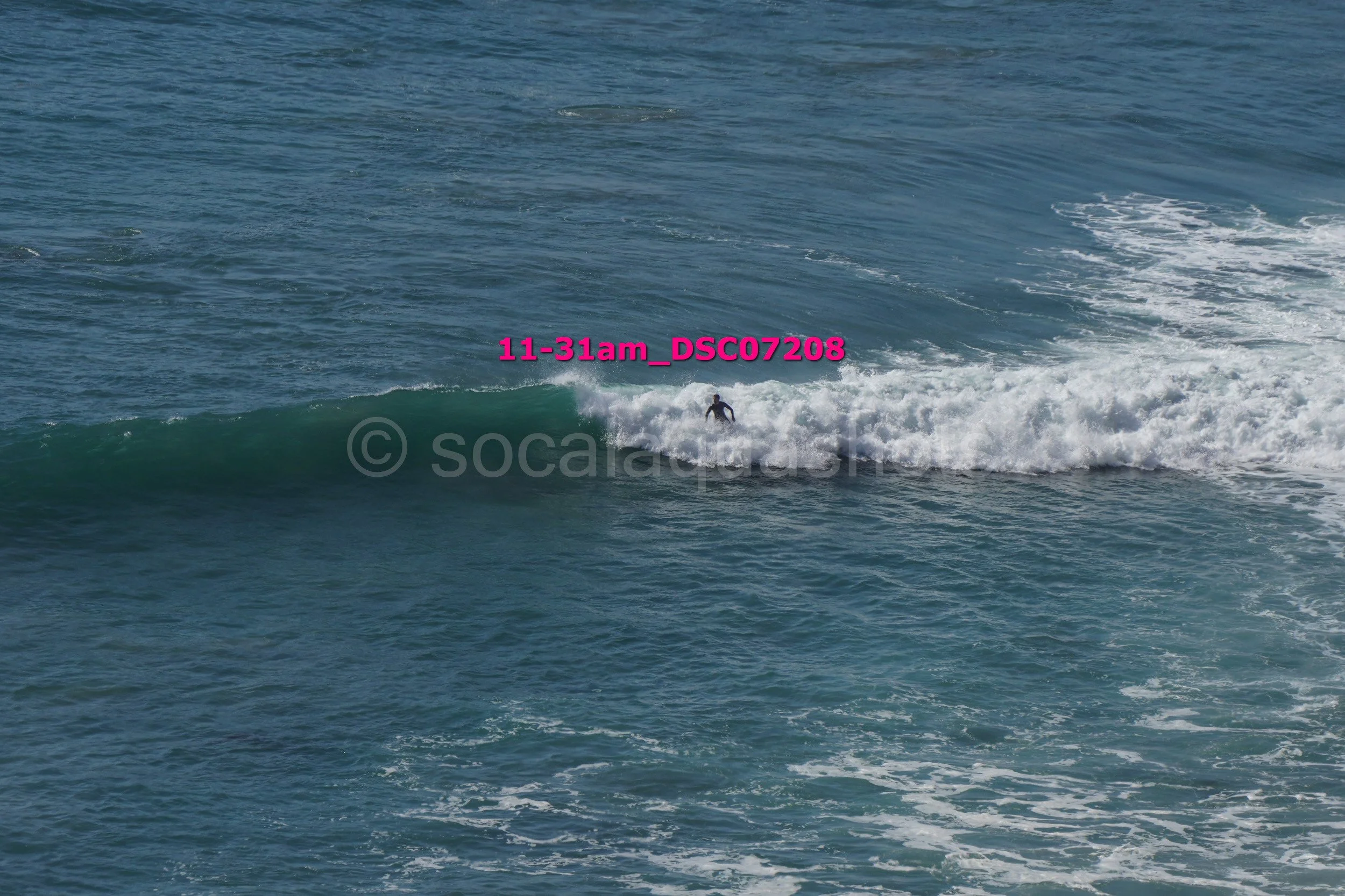 A person surfing on the ocean waves with blue water and white foam, with a watermark and a file name overlay.