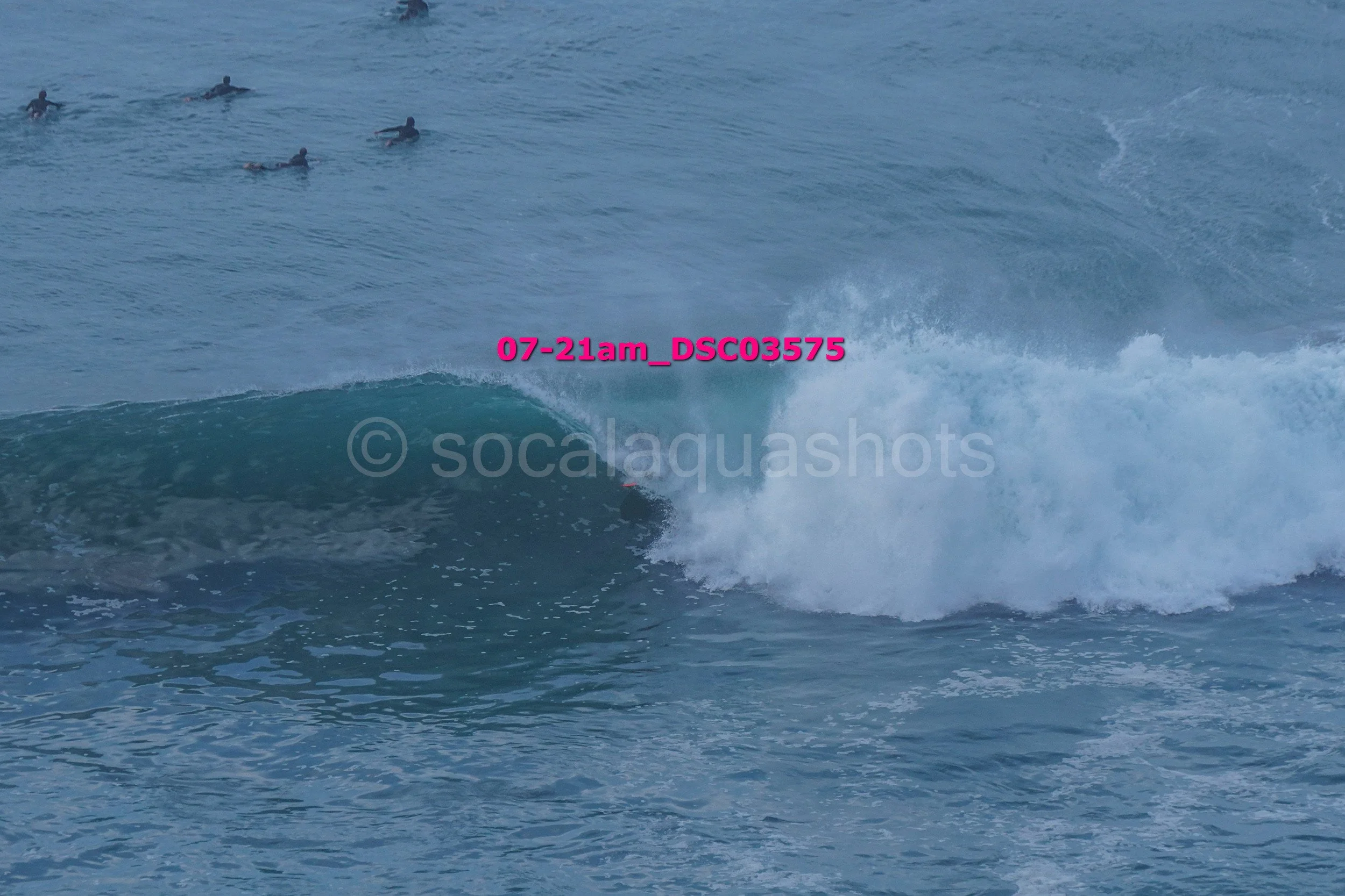 Surfer riding a wave with four other surfers in the distance in the ocean.