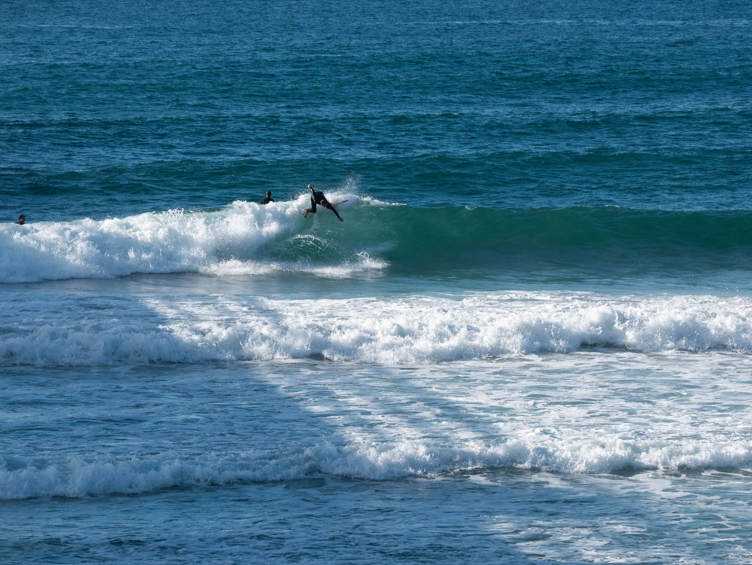 People surfing on ocean waves with blue water in the background.