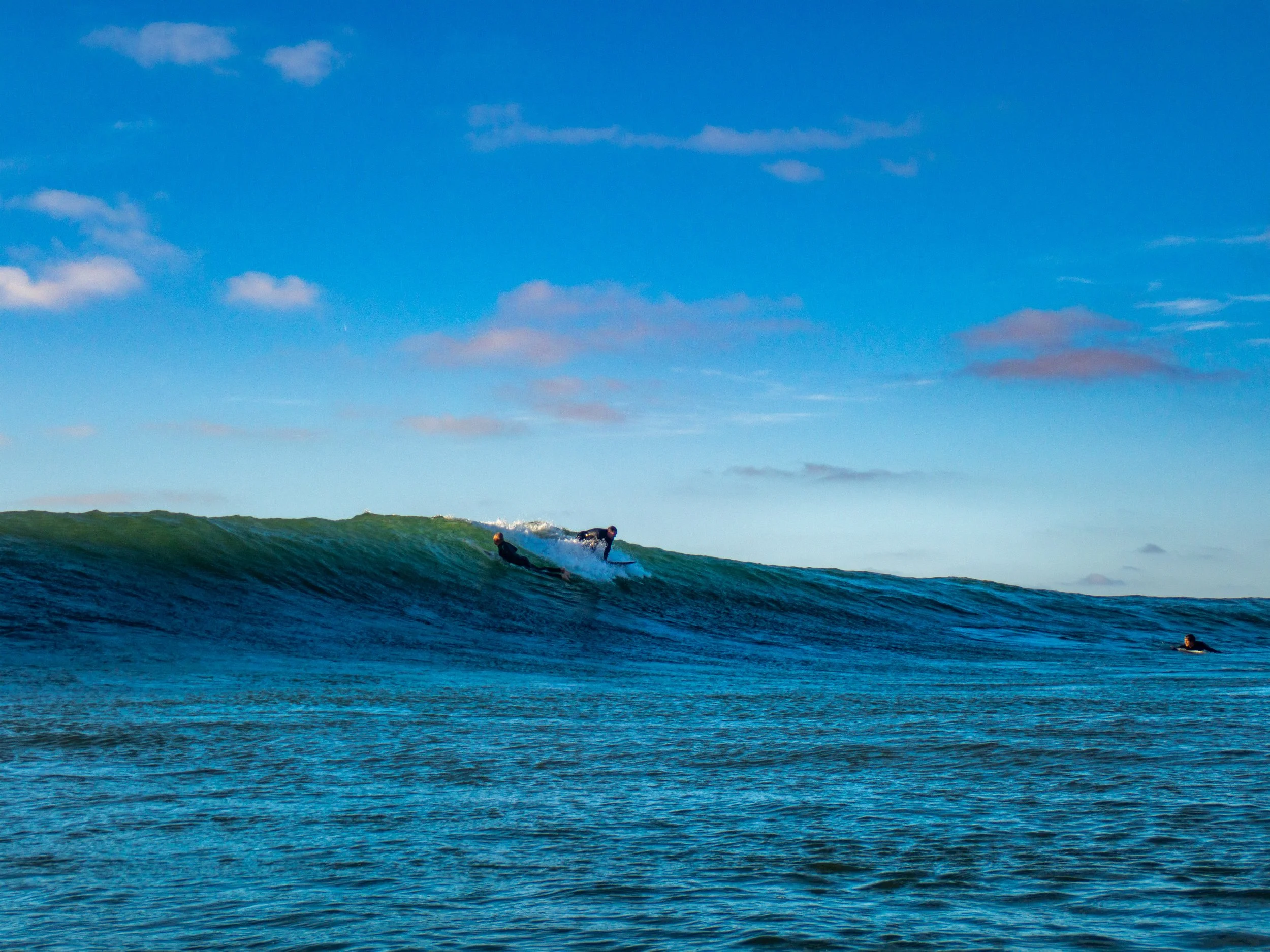 Two surfers riding a wave in the ocean under a partly cloudy sky.