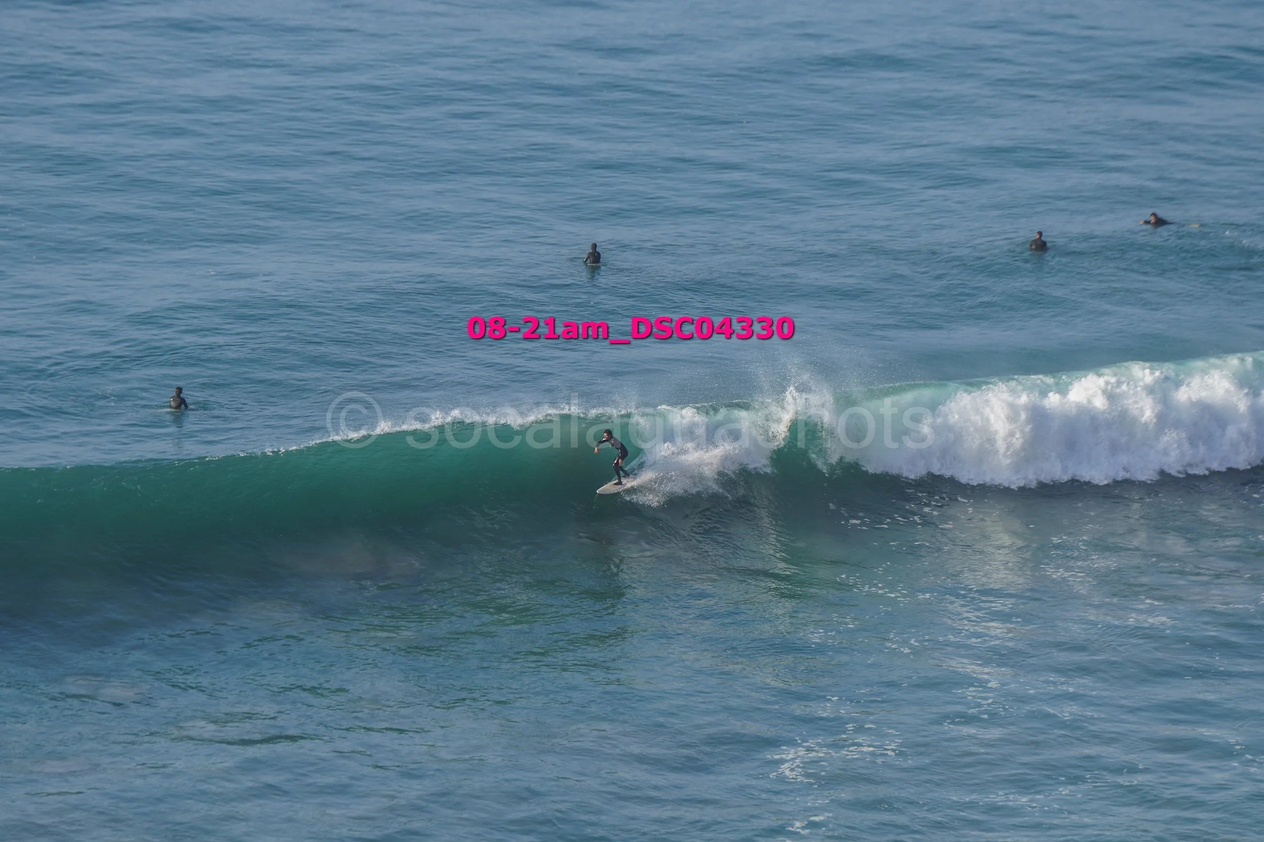 A person surfing on a wave in the ocean with several people swimming in the background.