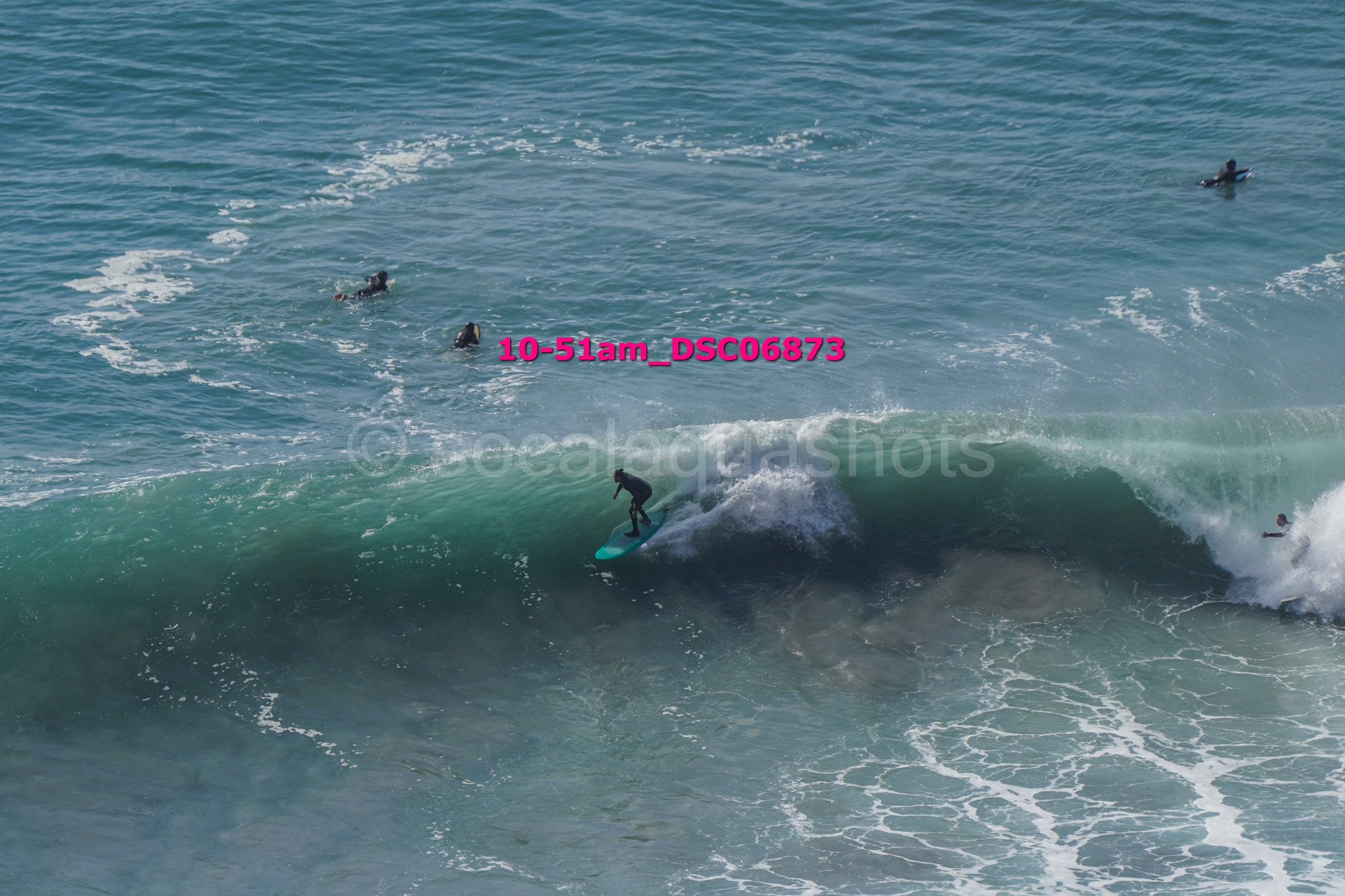 A person surfing on a wave in the ocean with several other surfers in the water nearby.
