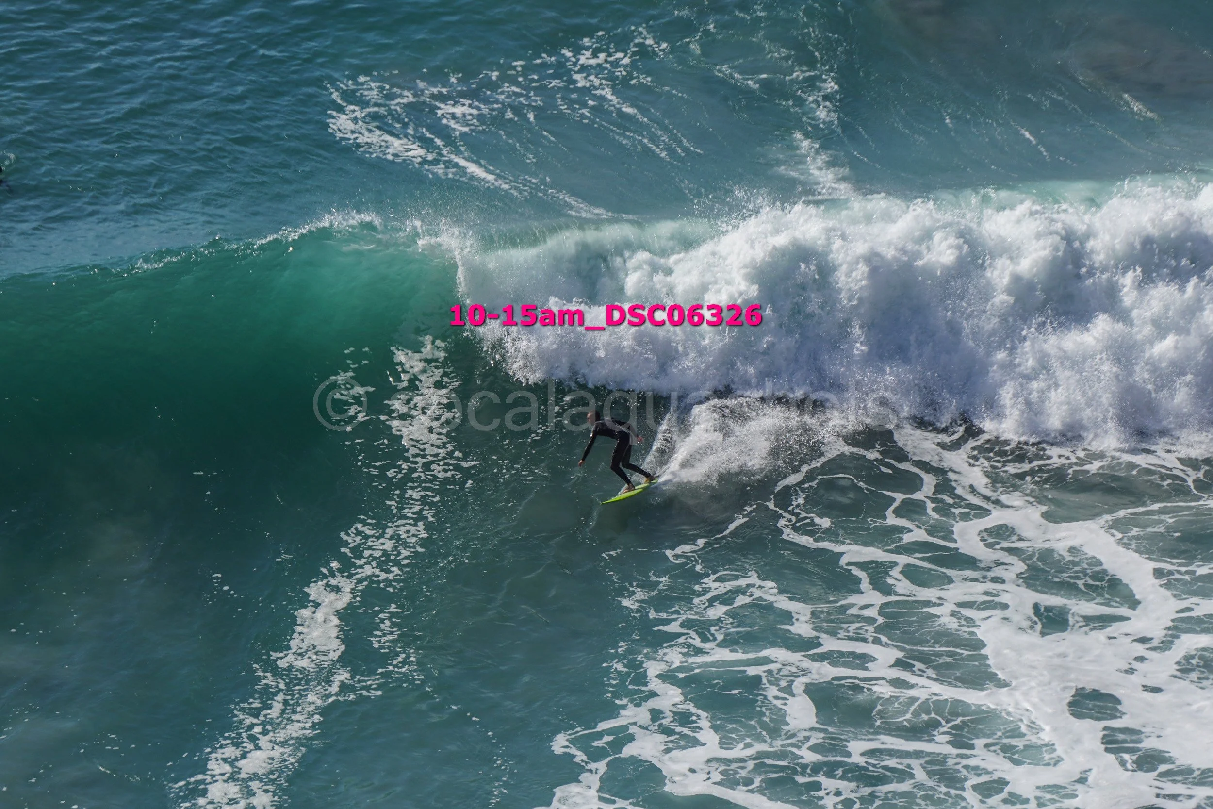 A person surfing on a large ocean wave with white foam and water spray.