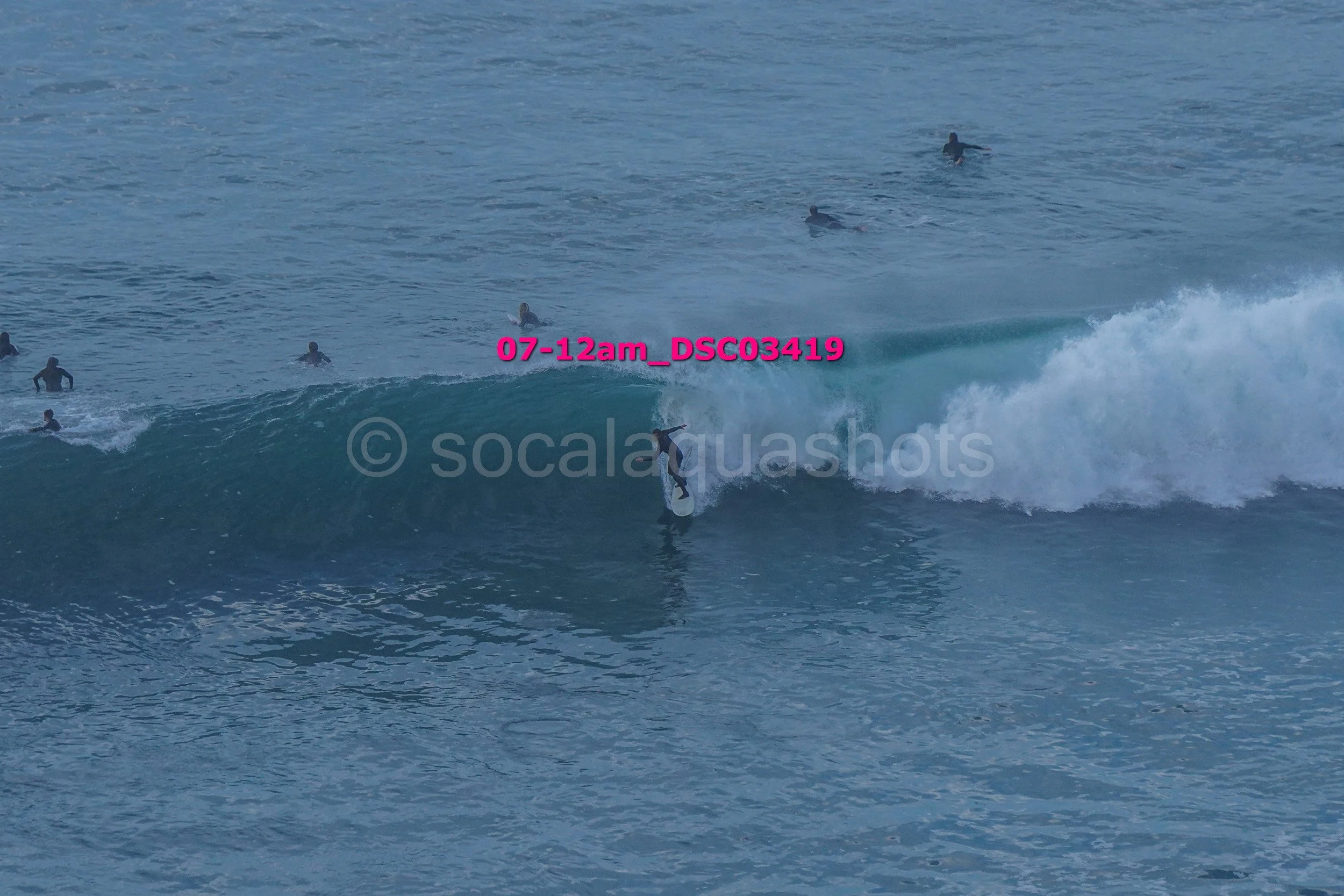 A person surfing on a wave with several surfers in the water in the background.