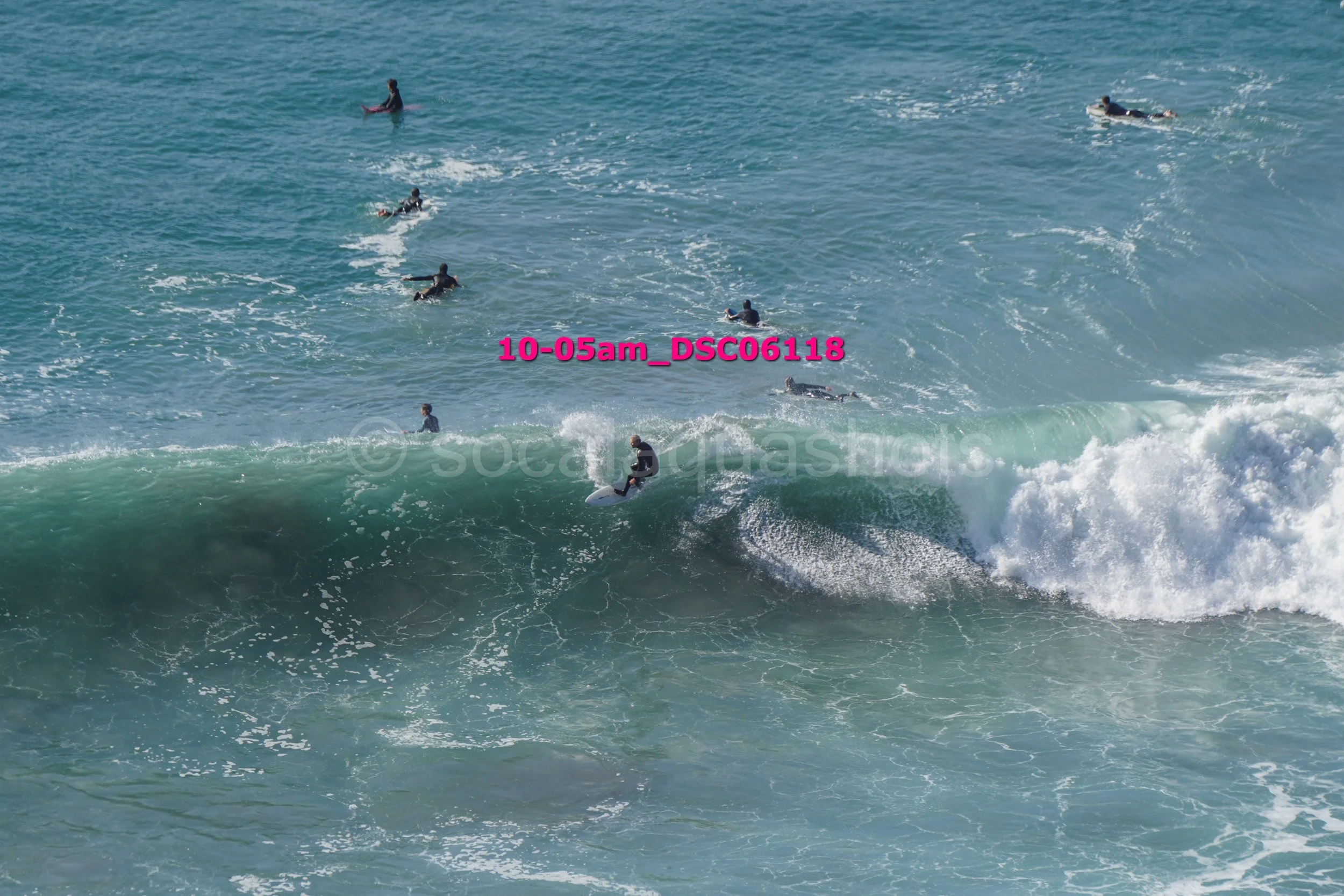 Surfers in the ocean, some paddling on surfboards, one riding a wave, during daytime.