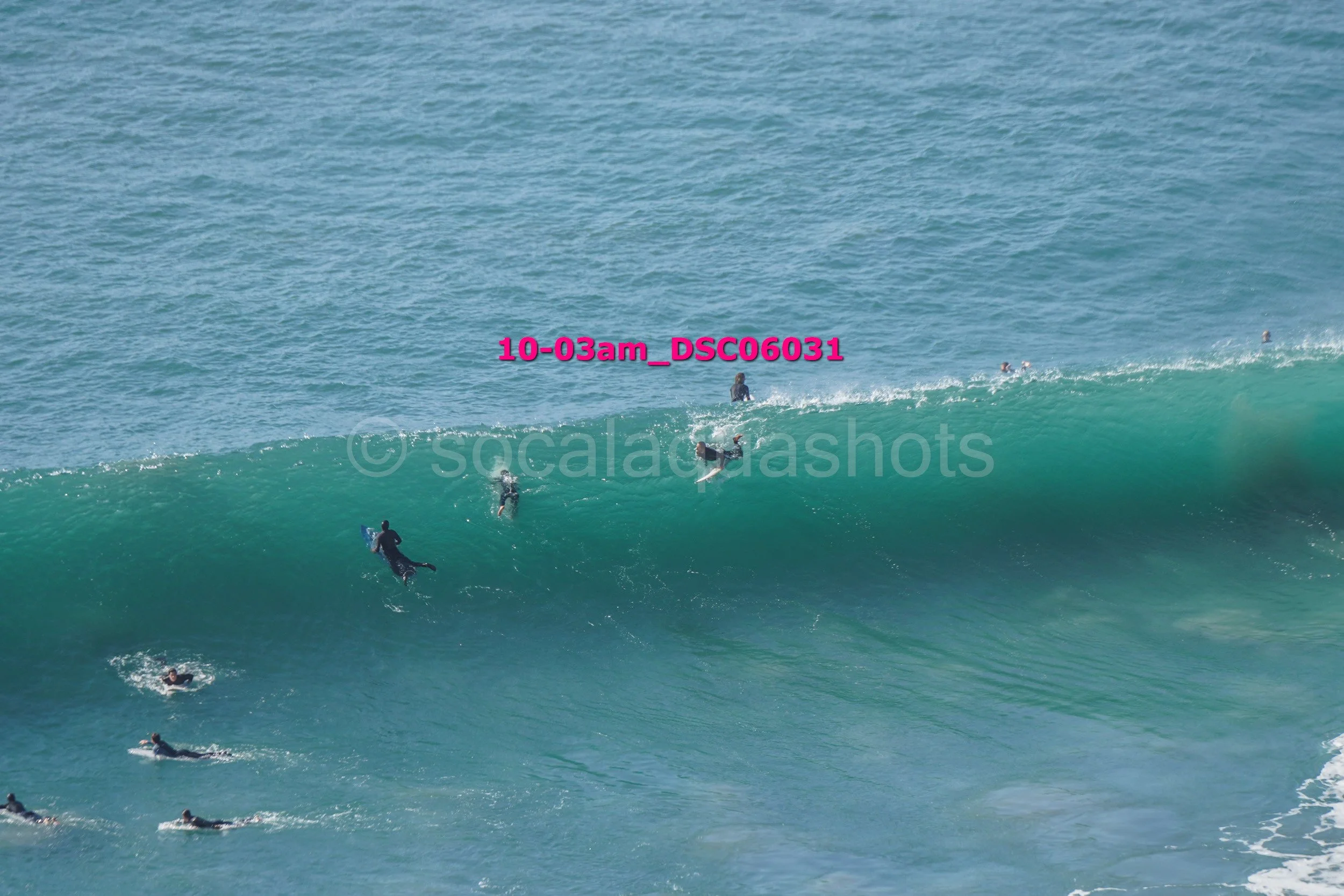 Multiple surfers riding a large ocean wave with the background showing blue water.