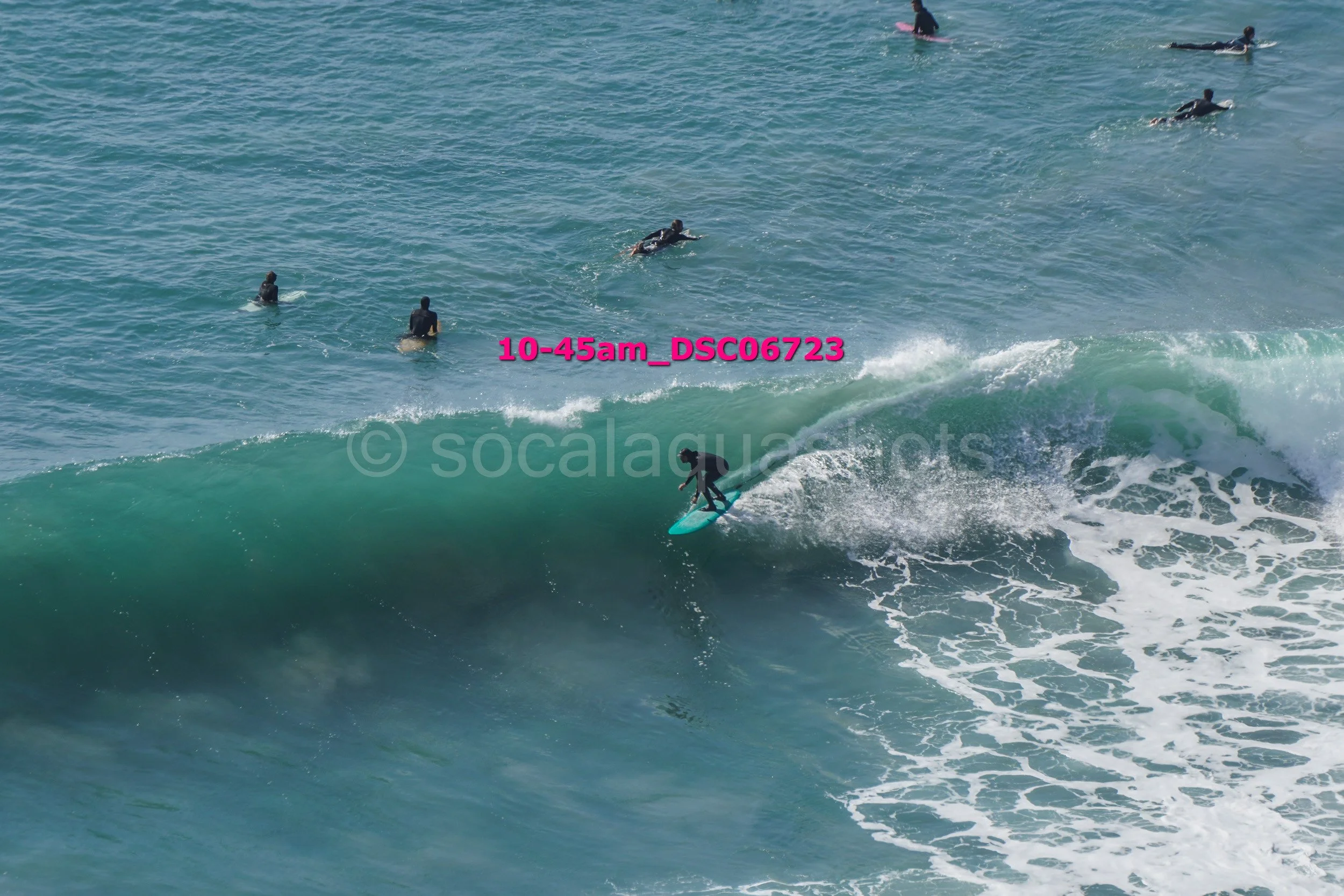 A person surfing a large wave while several people are swimming or surfing in the distance in the ocean.