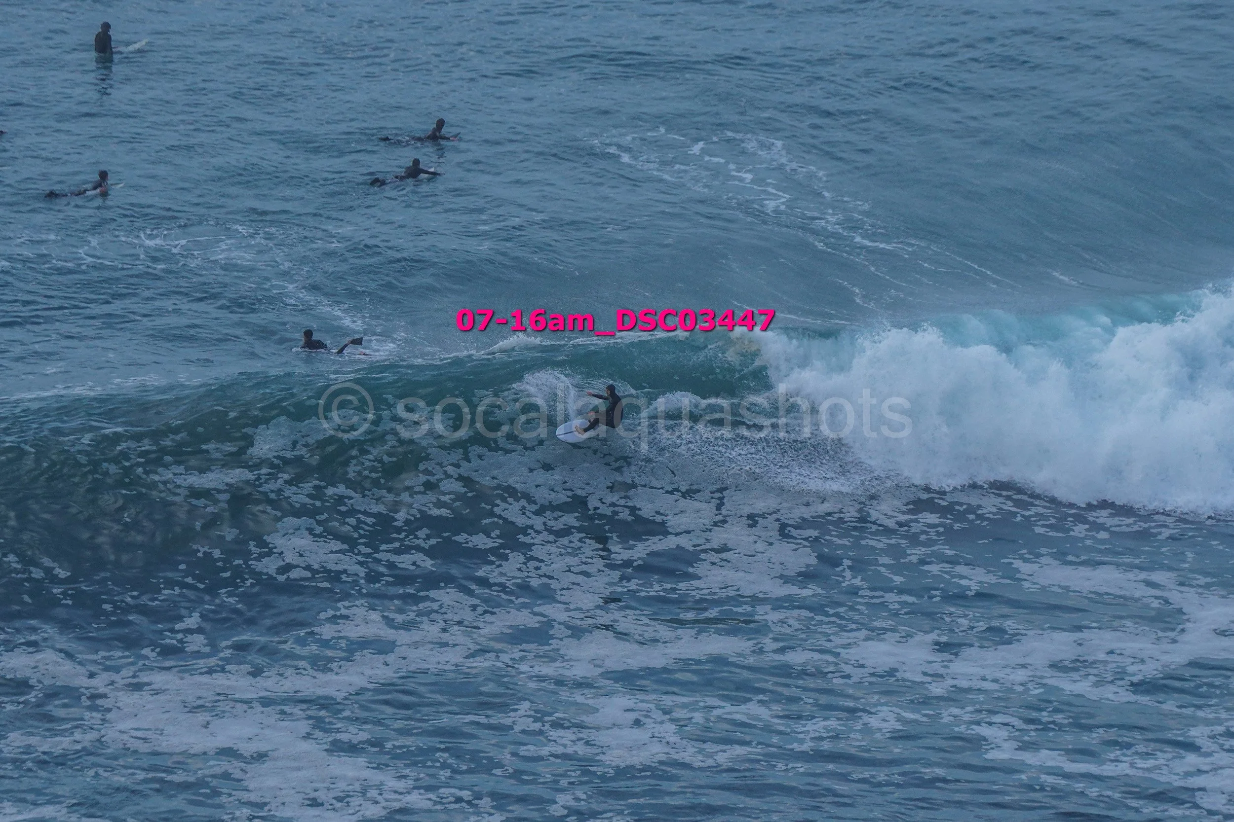 A group of people surfing on ocean waves, with some lying on surfboards and others paddling